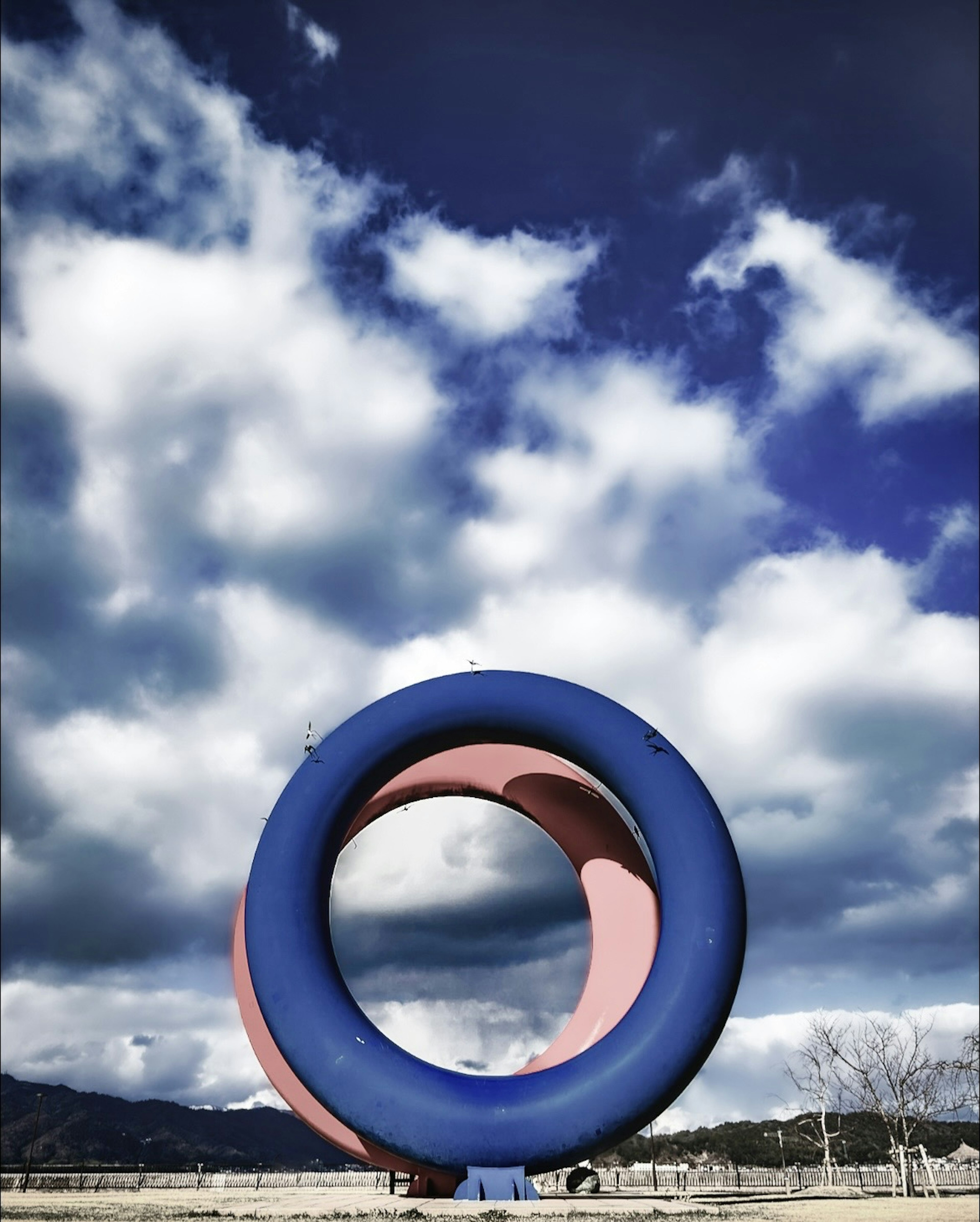 Blue circular sculpture against a backdrop of clouds