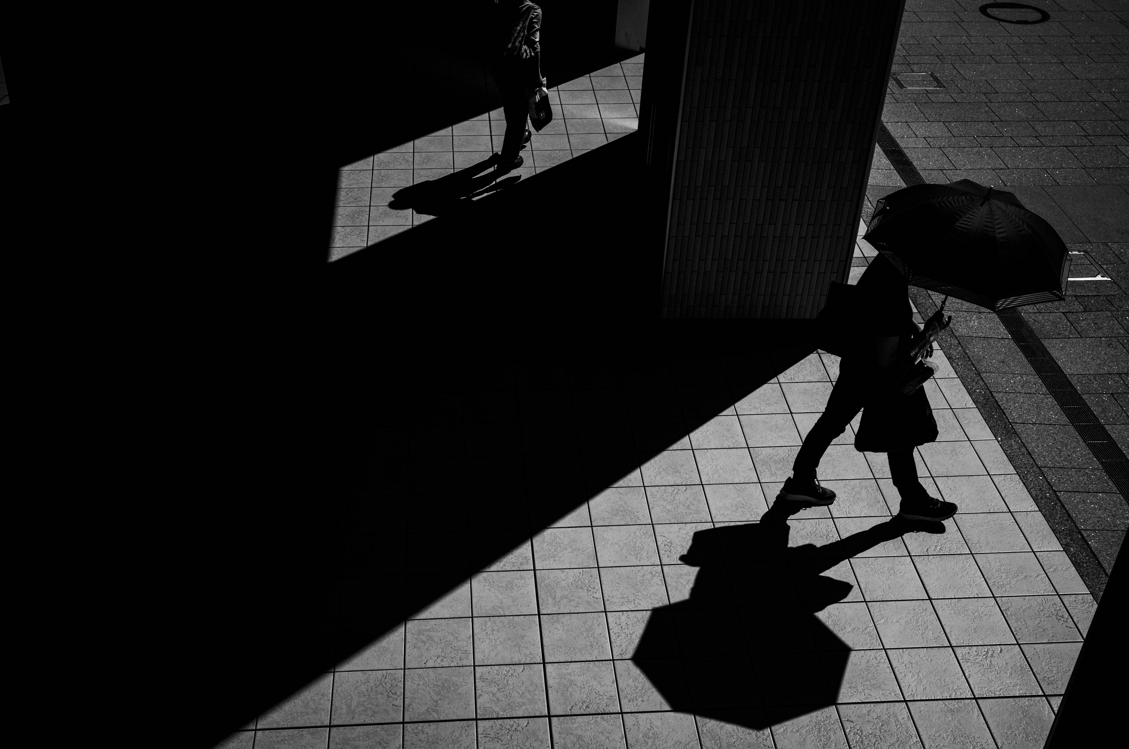 A person walking with an umbrella in dark shadows and surrounding silhouettes