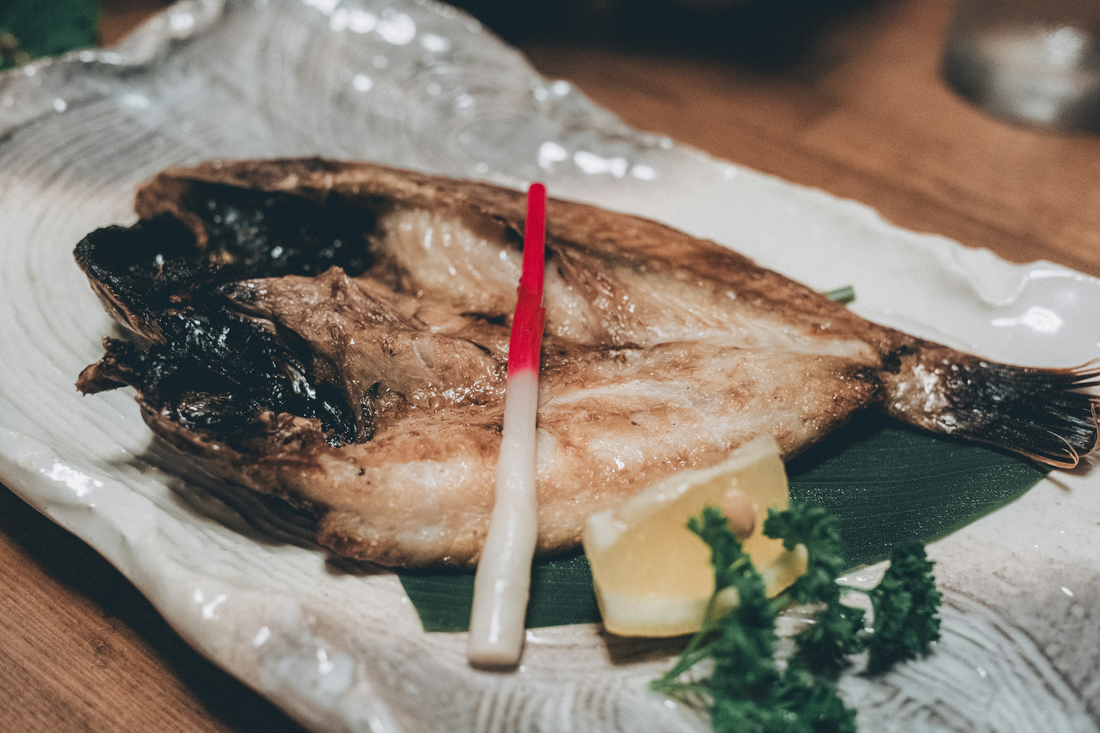 Gegrillter Fisch auf einem Teller mit Zitrone und Petersiliengarnitur serviert