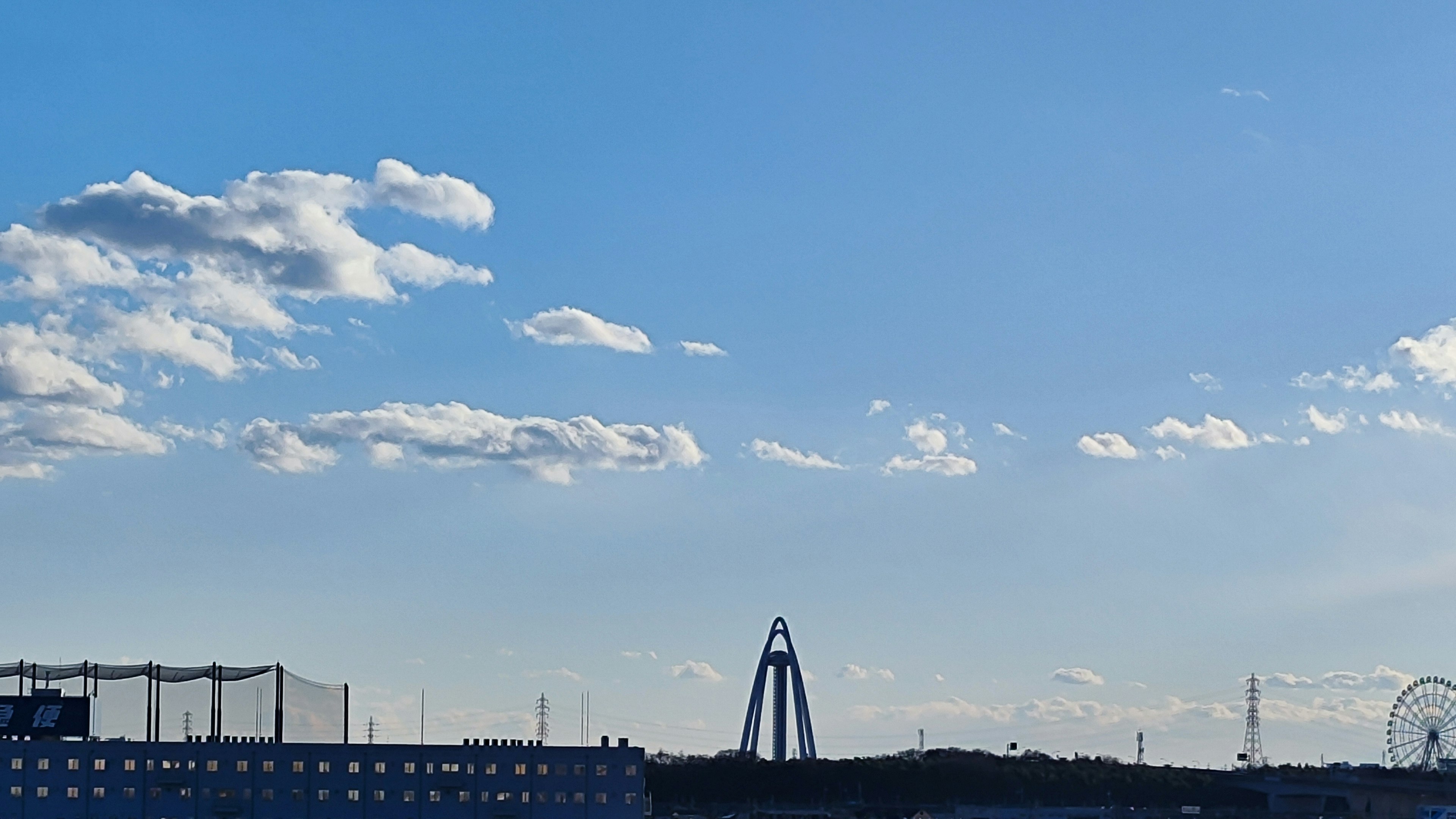 青空と雲が広がる風景に遊園地の観覧車が見える