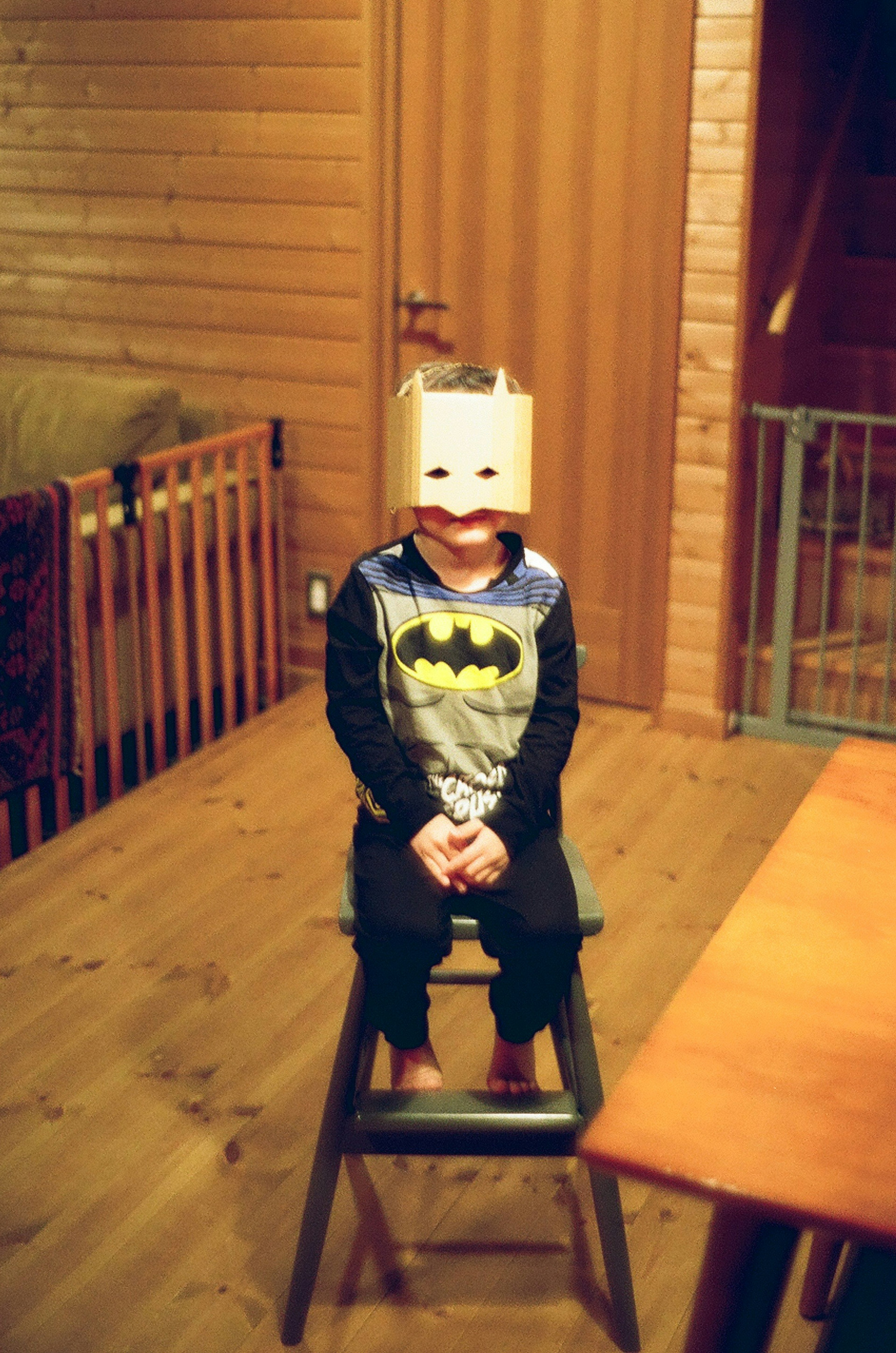 Child wearing Batman pajamas sitting on a stool in a wooden room