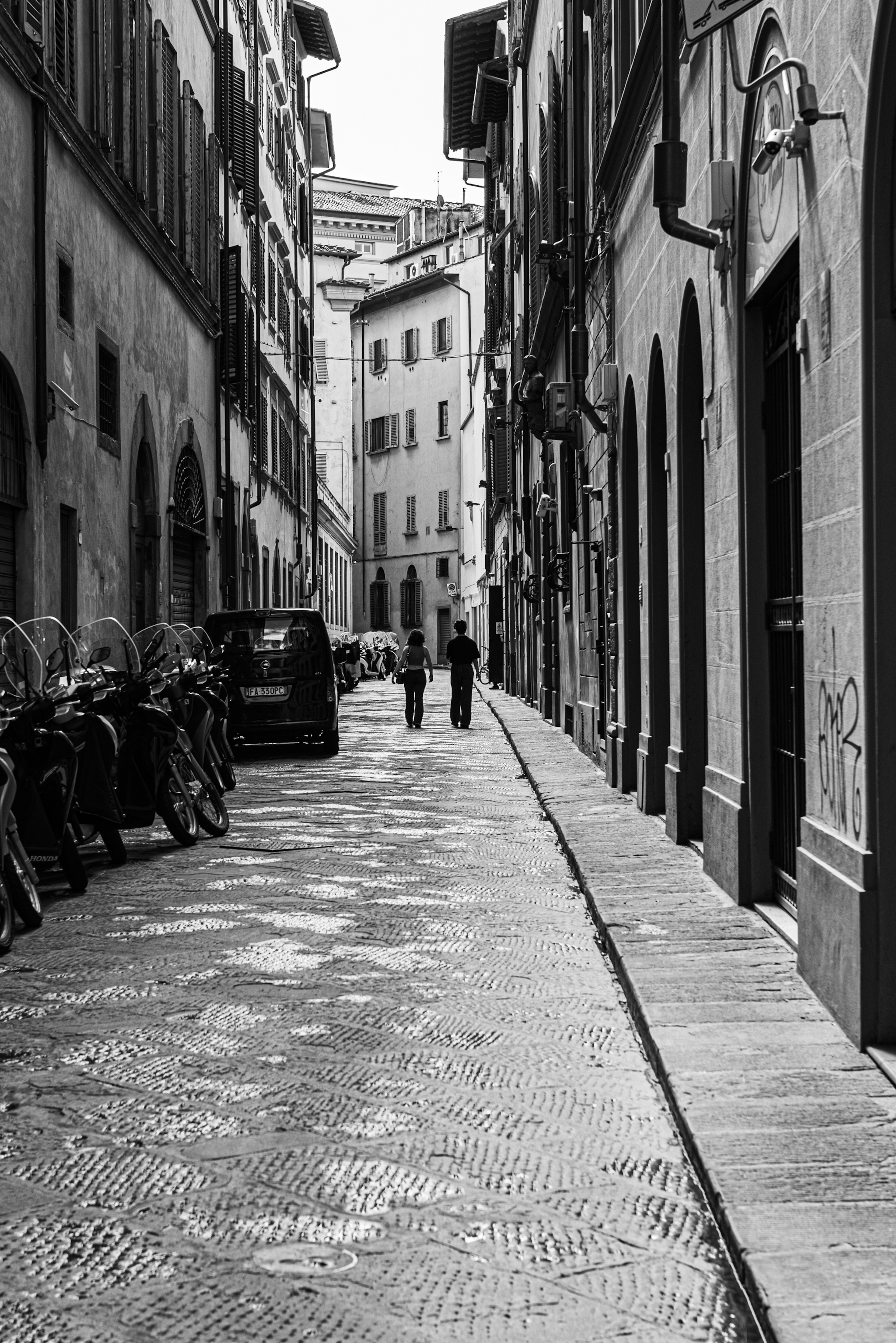 Narrow street in Florence with bicycles and pedestrians in black and white