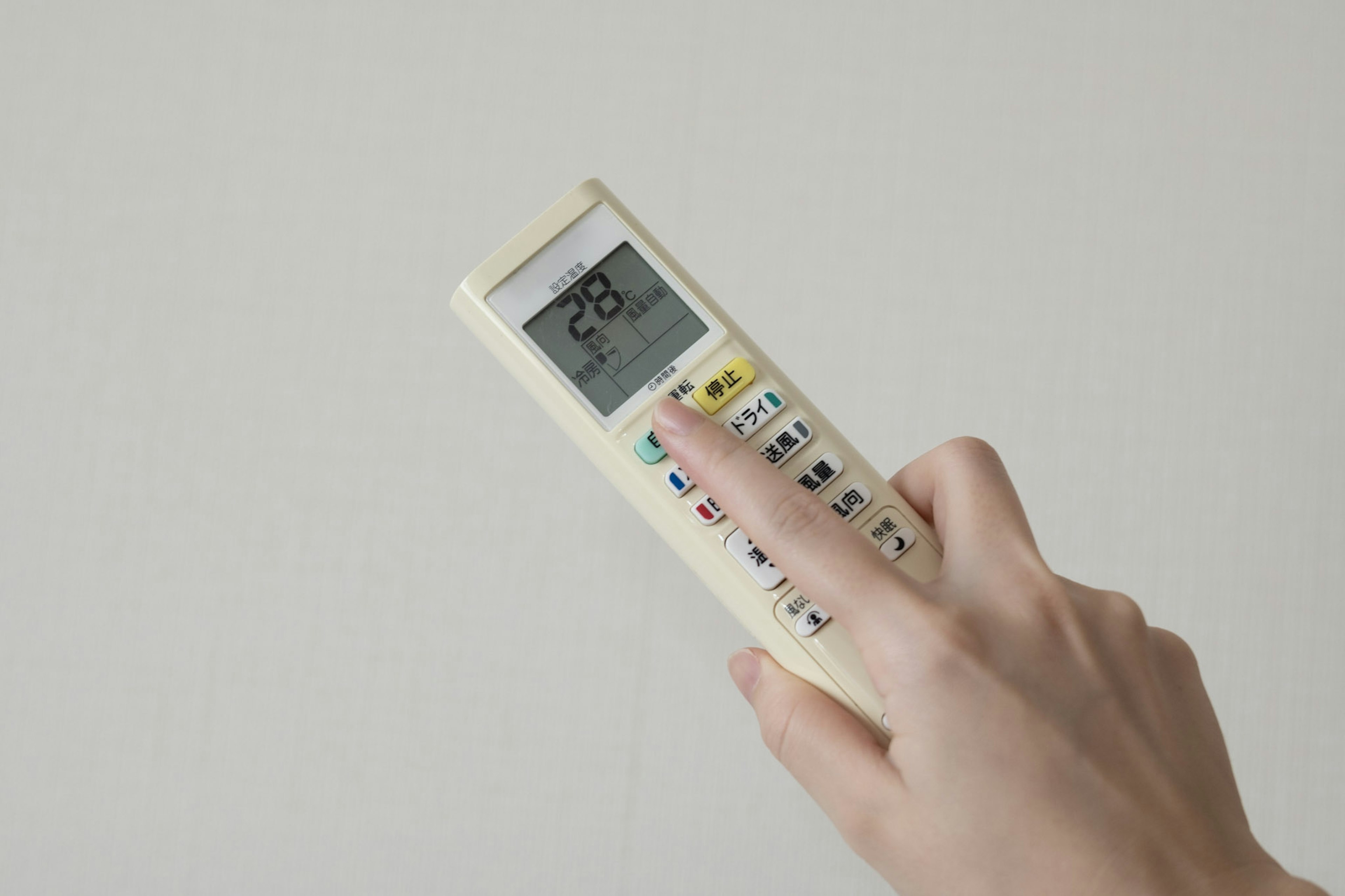 A hand holding a remote control displaying 28 degrees against a simple background