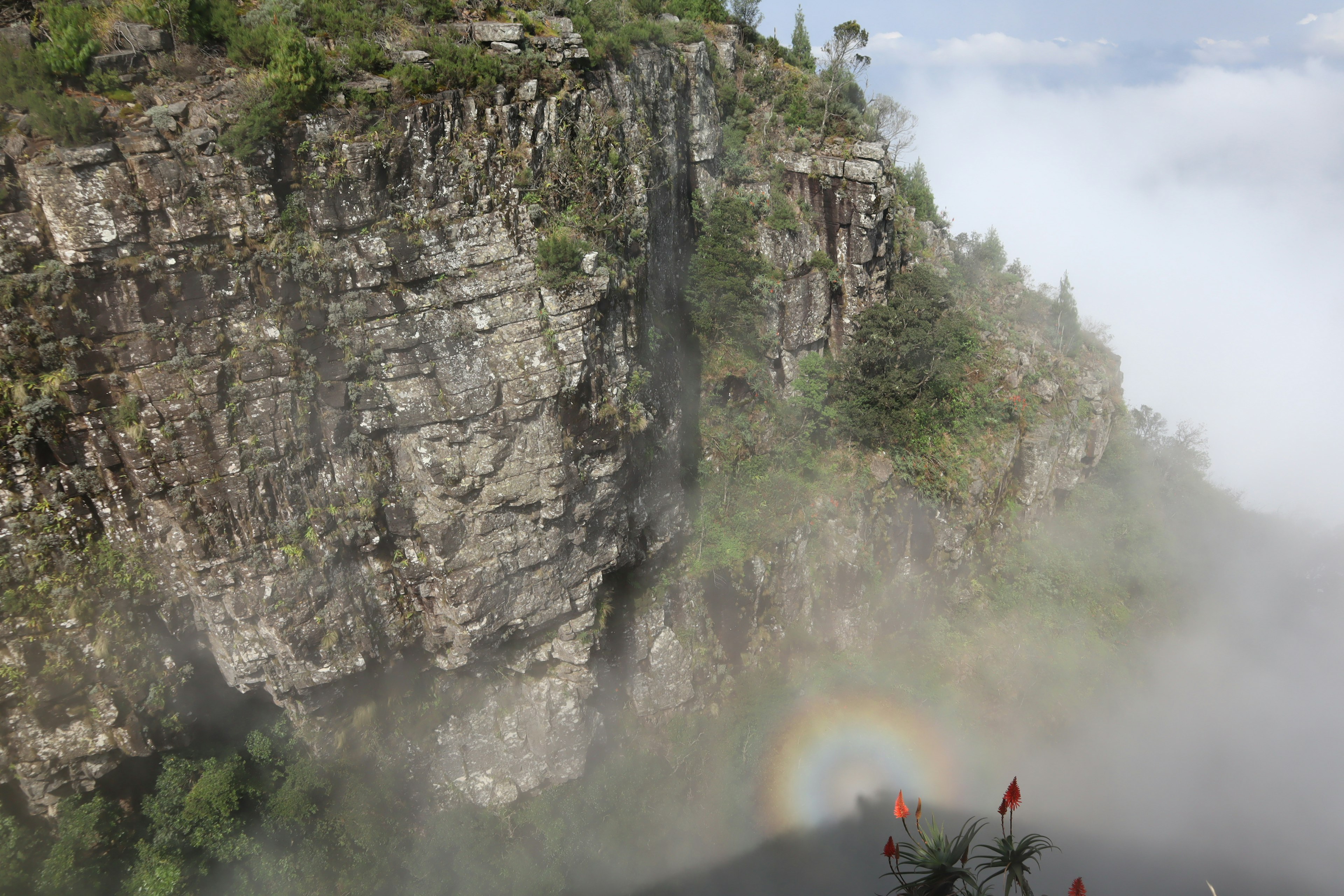 Scogliera con cascata circondata da nebbia con un arcobaleno