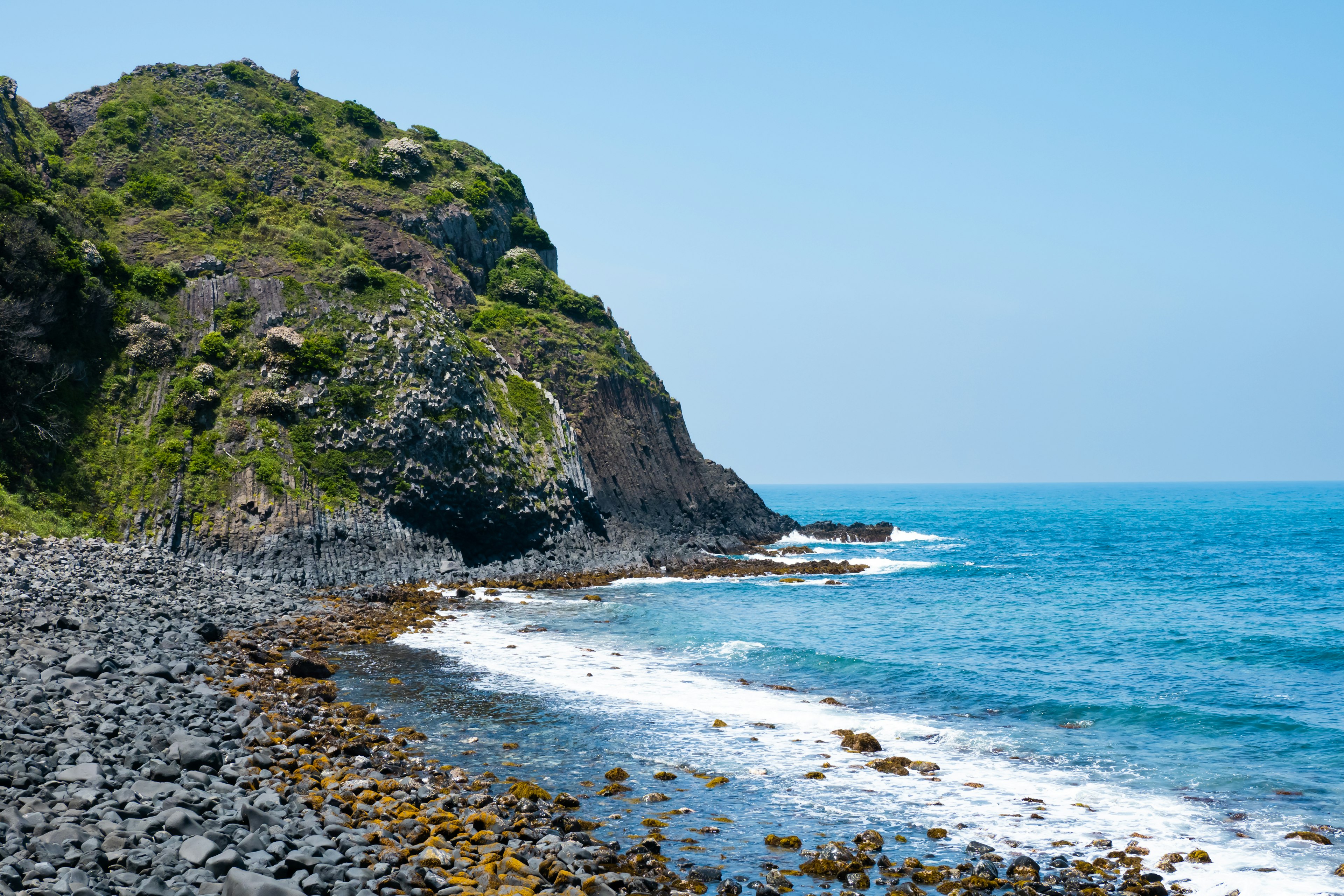 Pemandangan indah pantai berbatu dengan lautan biru dan bukit hijau subur