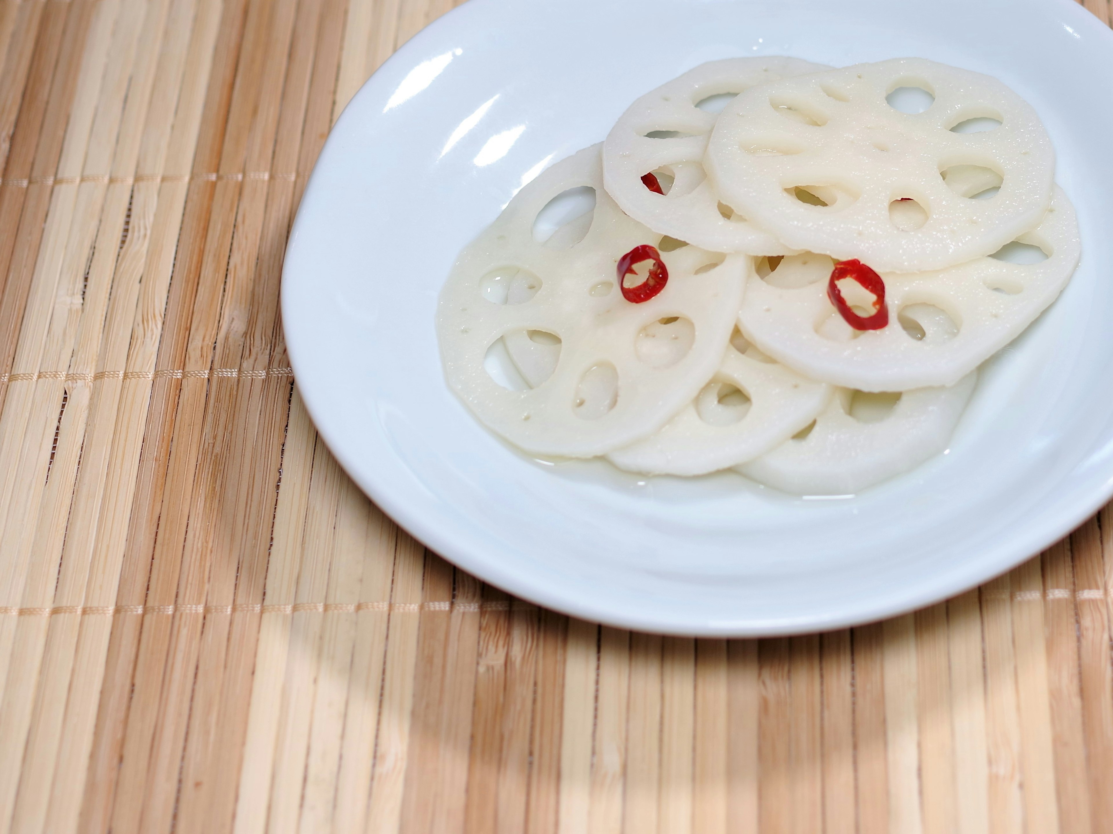 Fette di radice di loto con peperoncino rosso su un piatto bianco