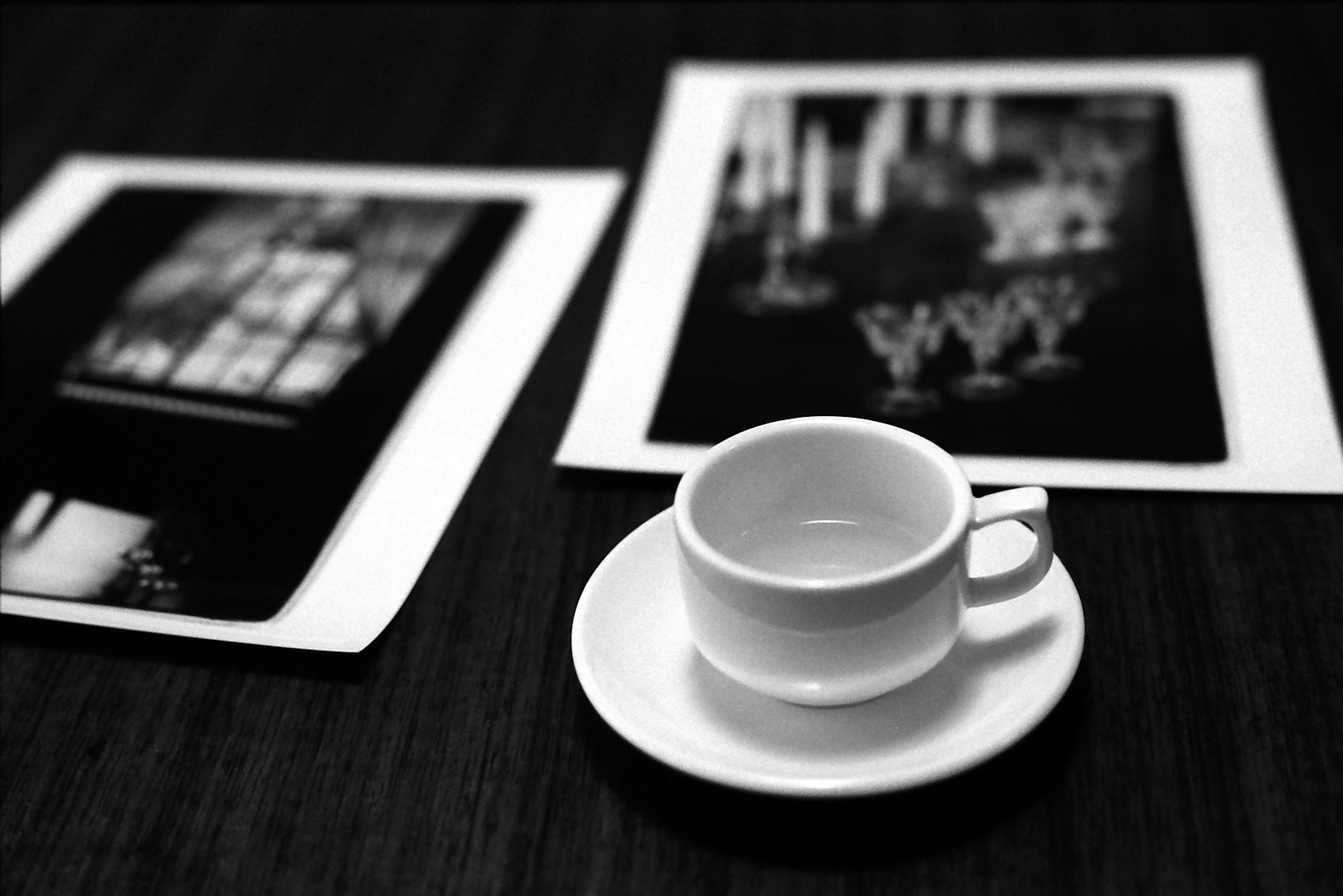 A white coffee cup on a saucer placed on a table with monochrome photographs nearby