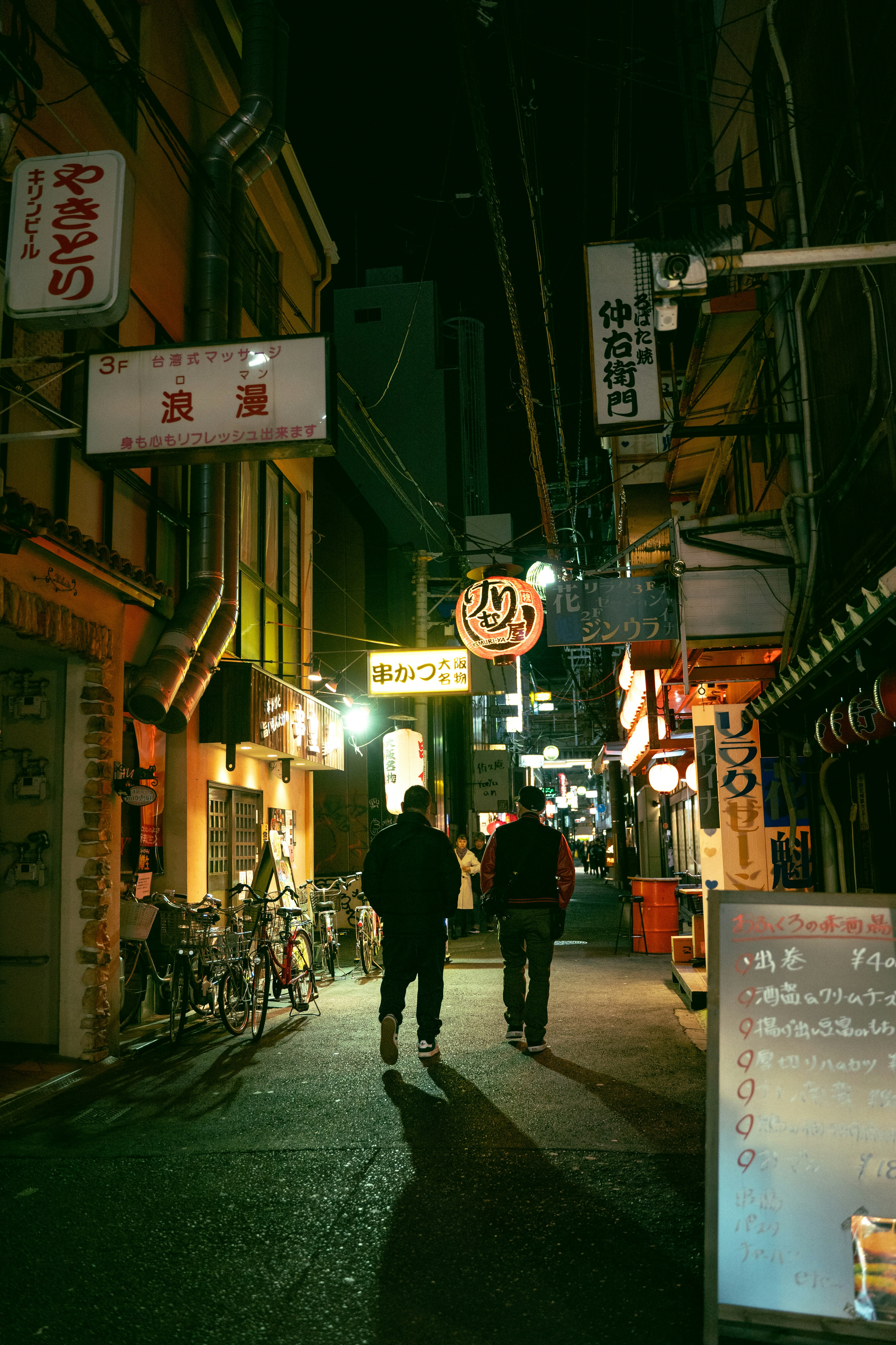 夜の街並みを歩く二人の人物とネオンの看板