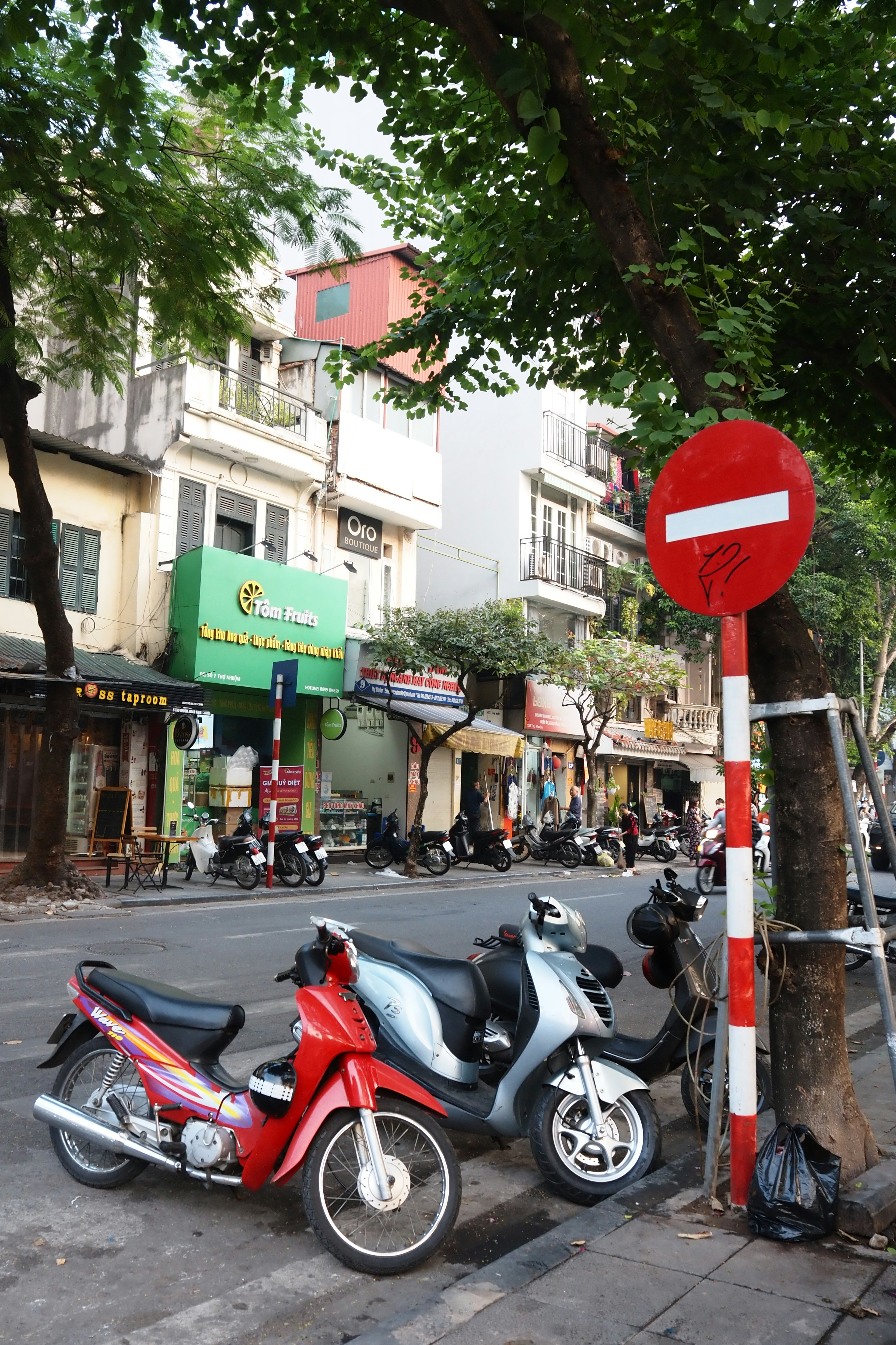 Street scene featuring a red scooter and a blue scooter parked near a no entry sign