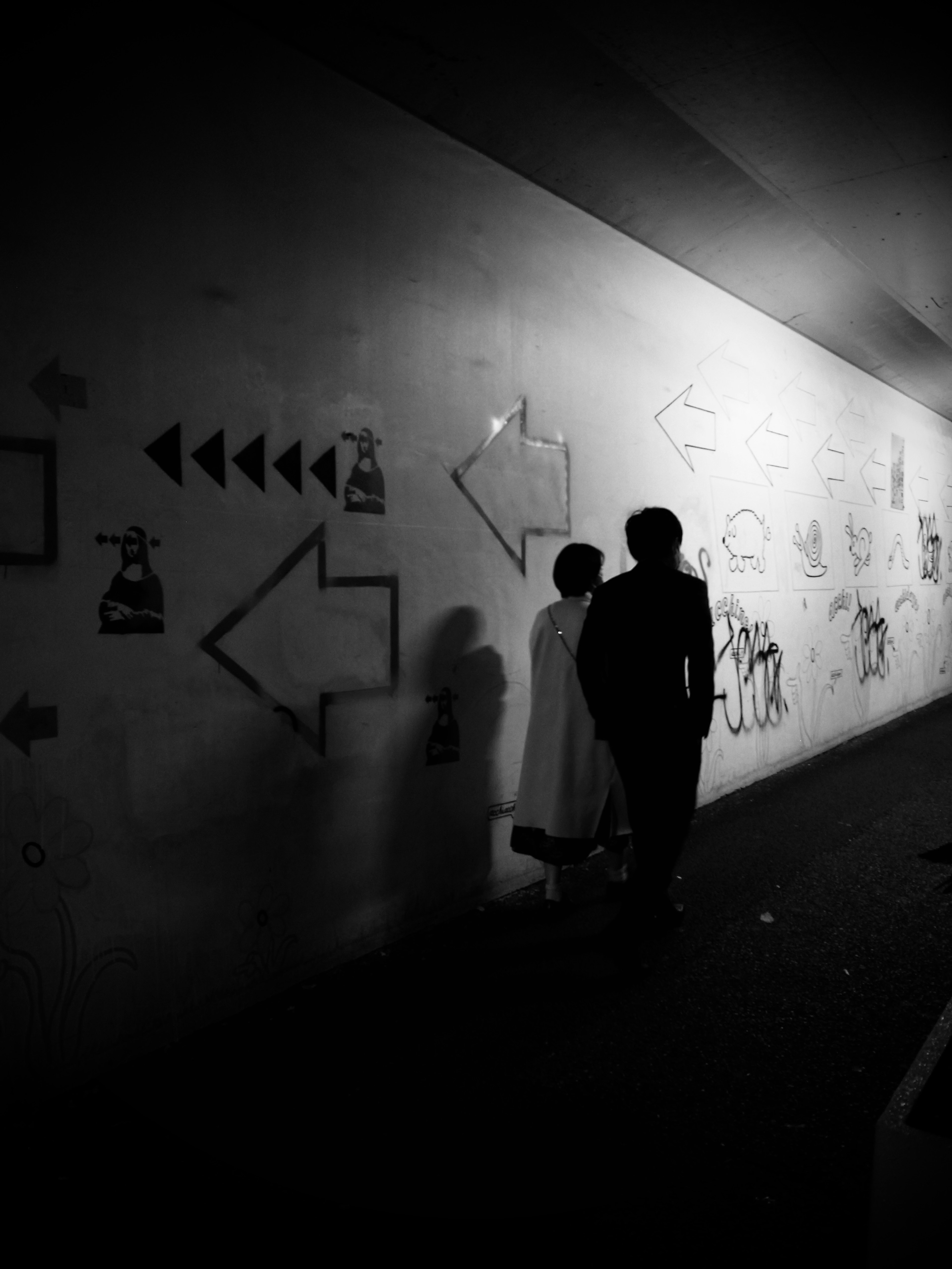 Silhouettes de deux personnes se tenant devant des graffitis et des flèches sur un mur sombre de tunnel