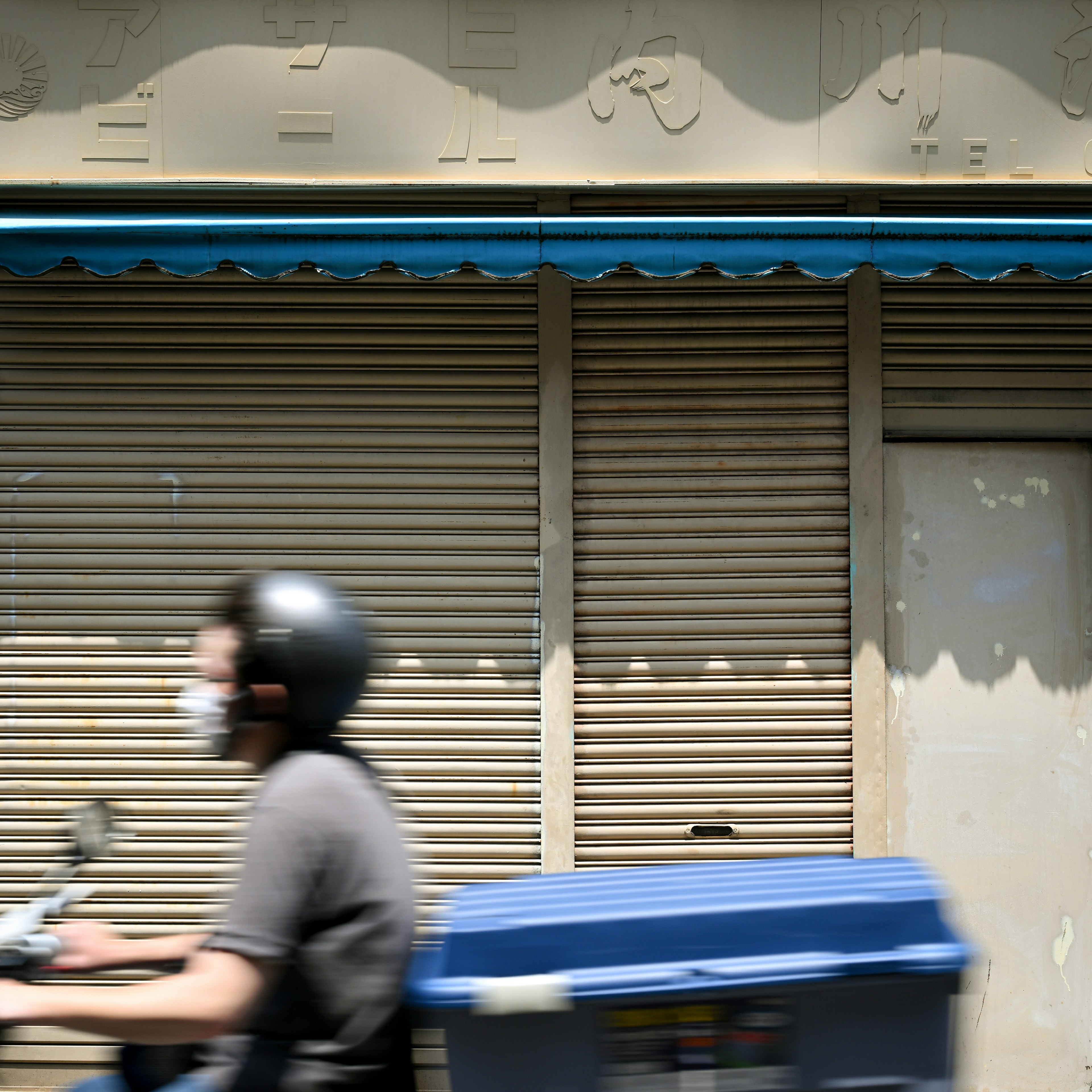 Repartidor pasando por una tienda cerrada con un toldo azul