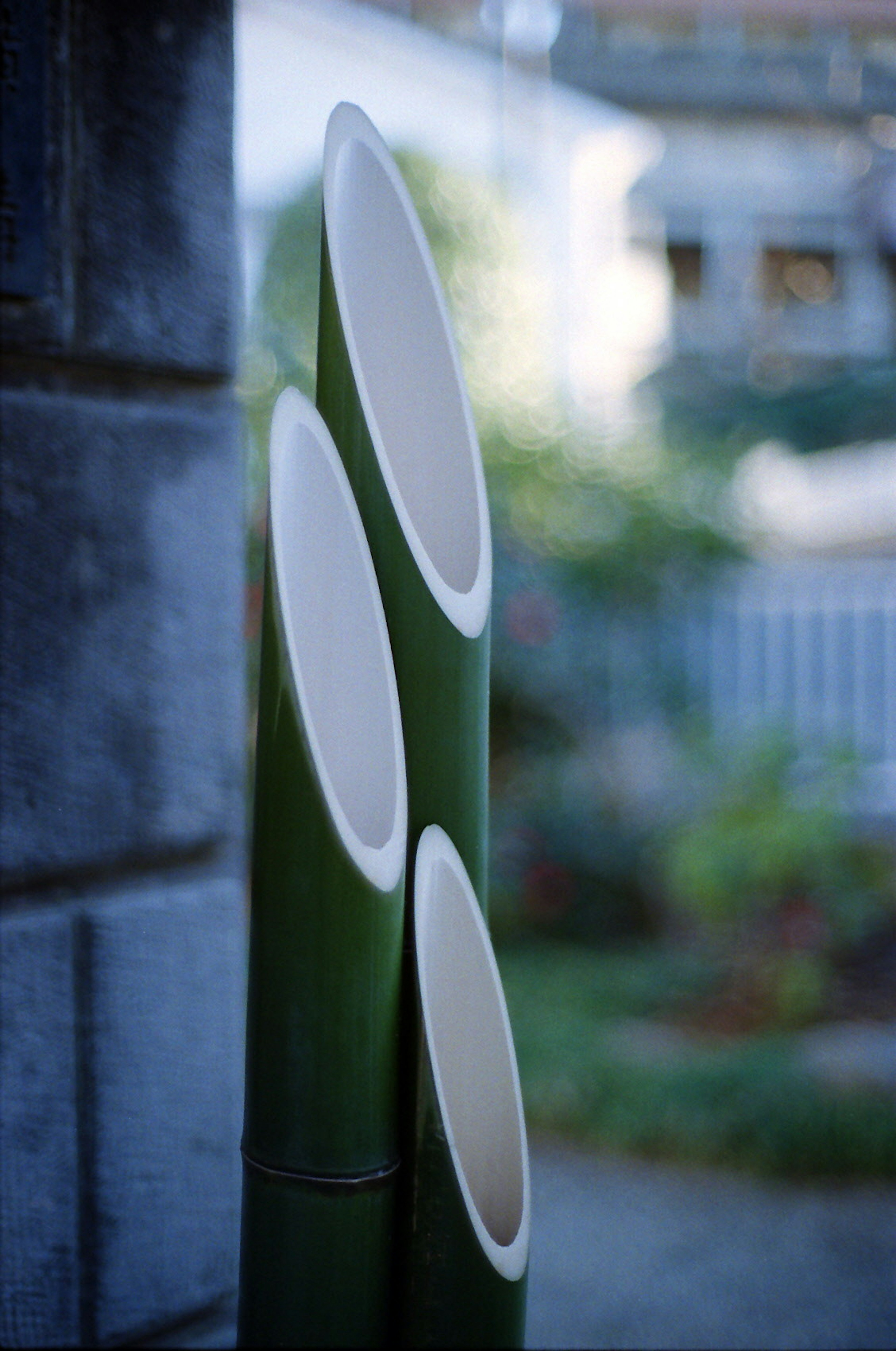 Three green bamboo tubes positioned against a blurred garden background