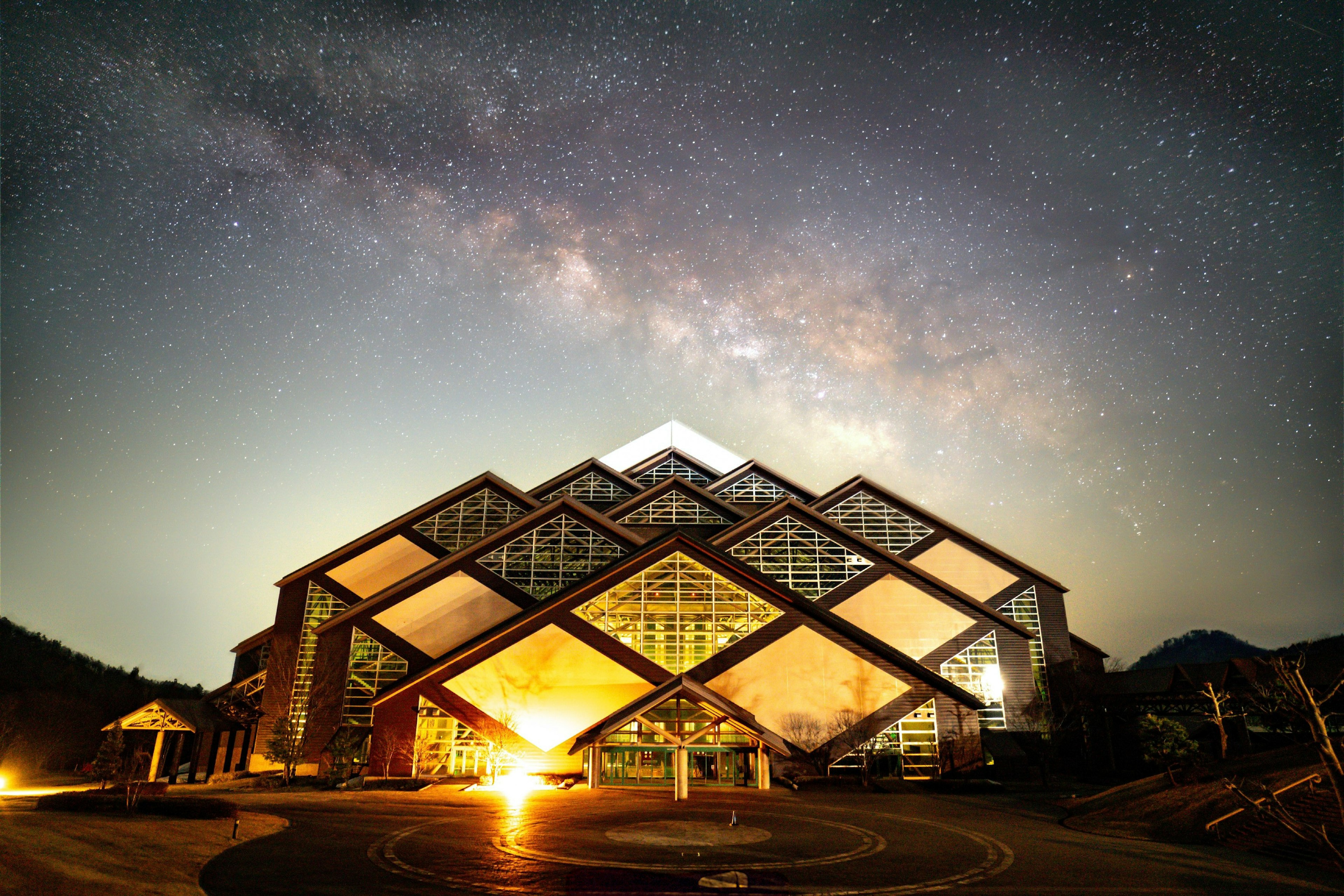 Bâtiment moderne sous un ciel étoilé avec des fenêtres lumineuses et un toit triangulaire