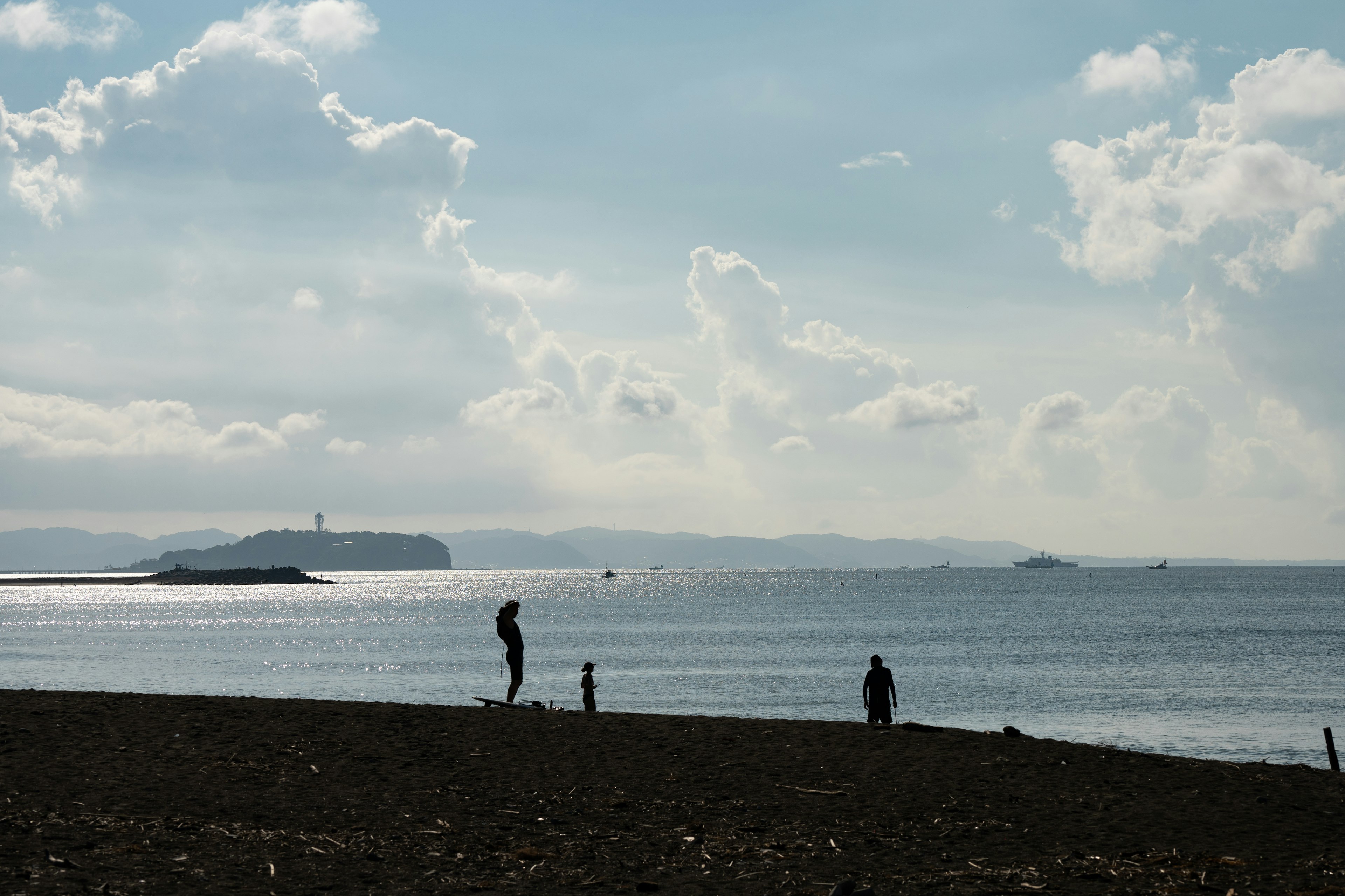 Silhouettes de personnes sur une plage avec une mer calme et des îles lointaines