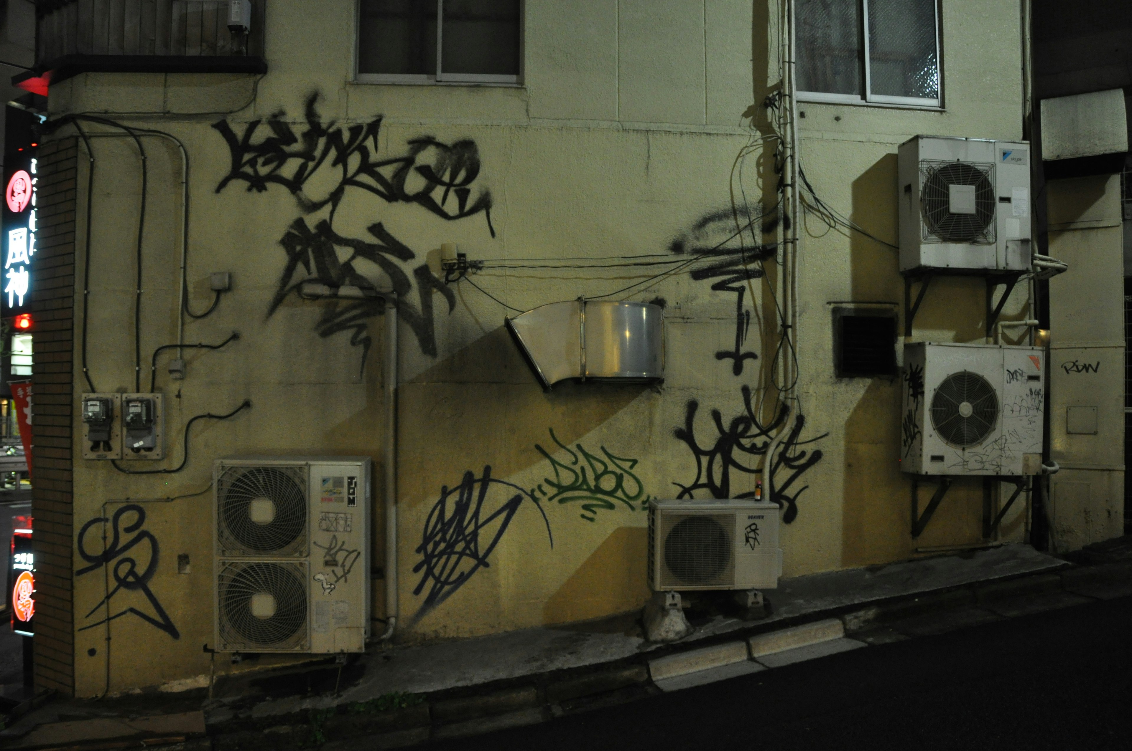 Graffiti on a wall with air conditioning units in a dimly lit area