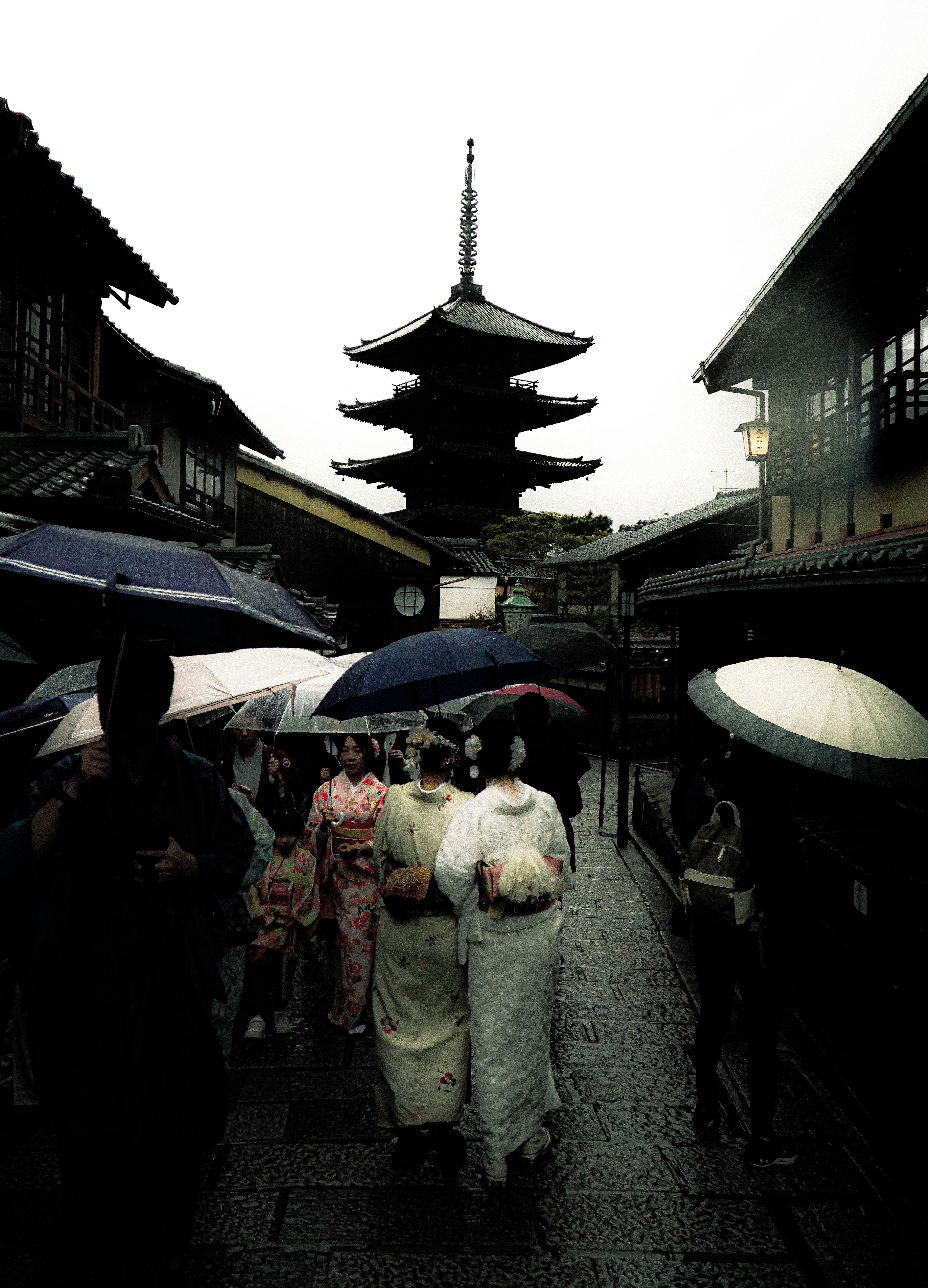 People in kimonos with umbrellas walking in the rain near a pagoda