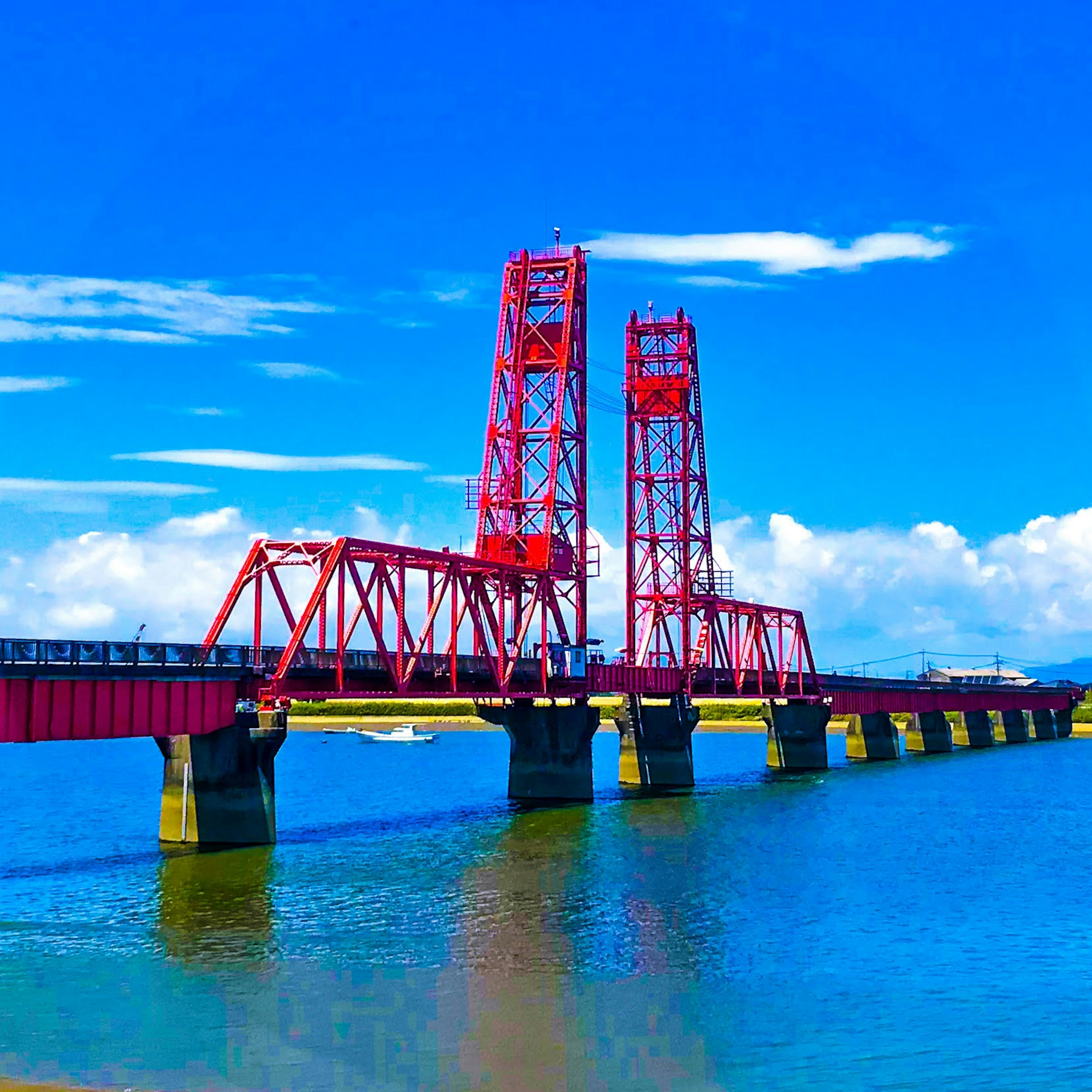 Red steel bridge over calm blue water under a clear sky