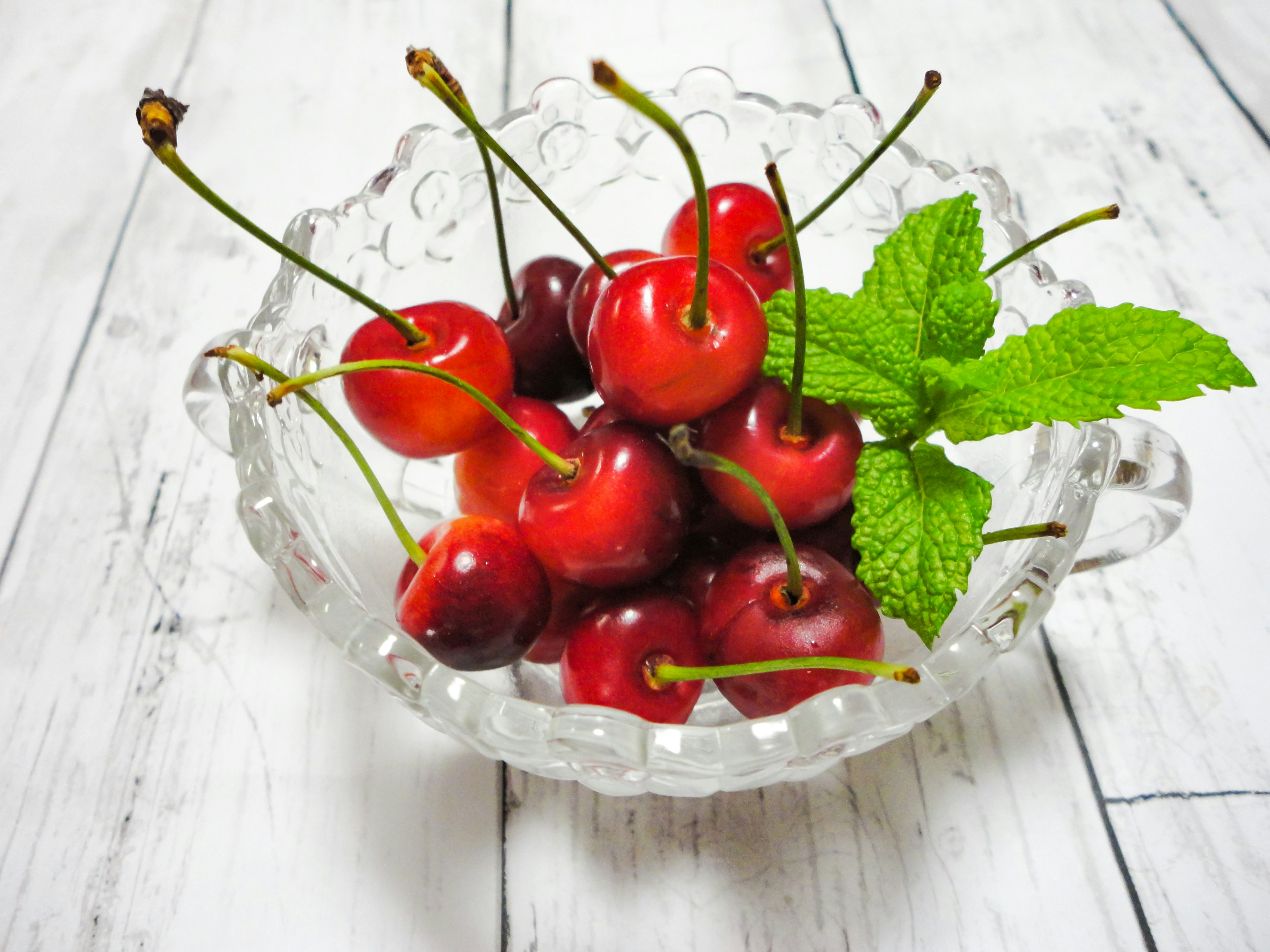 Cerezas frescas y hojas de menta en un tazón de cristal