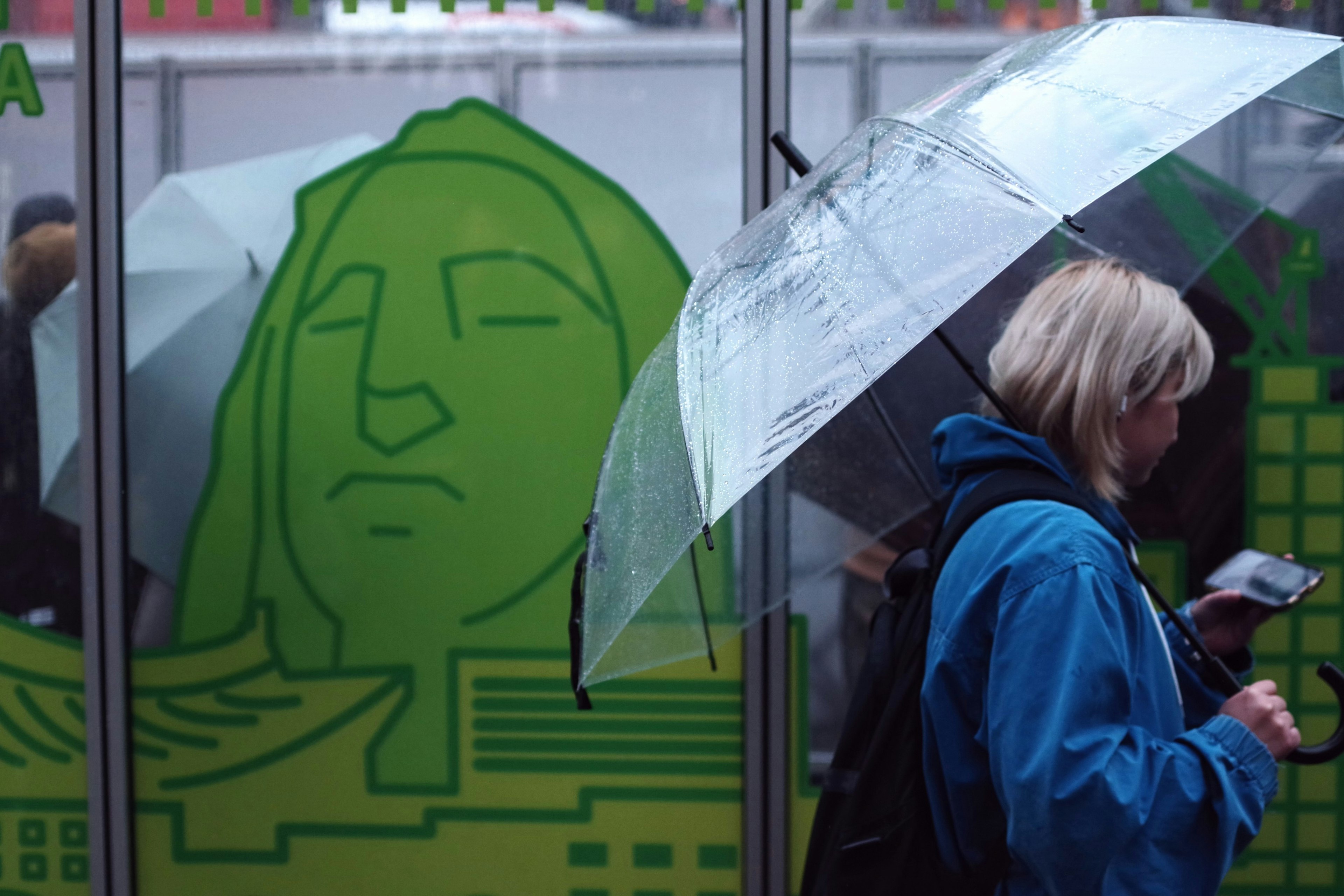 Una mujer con un paraguas transparente caminando frente a un mural verde