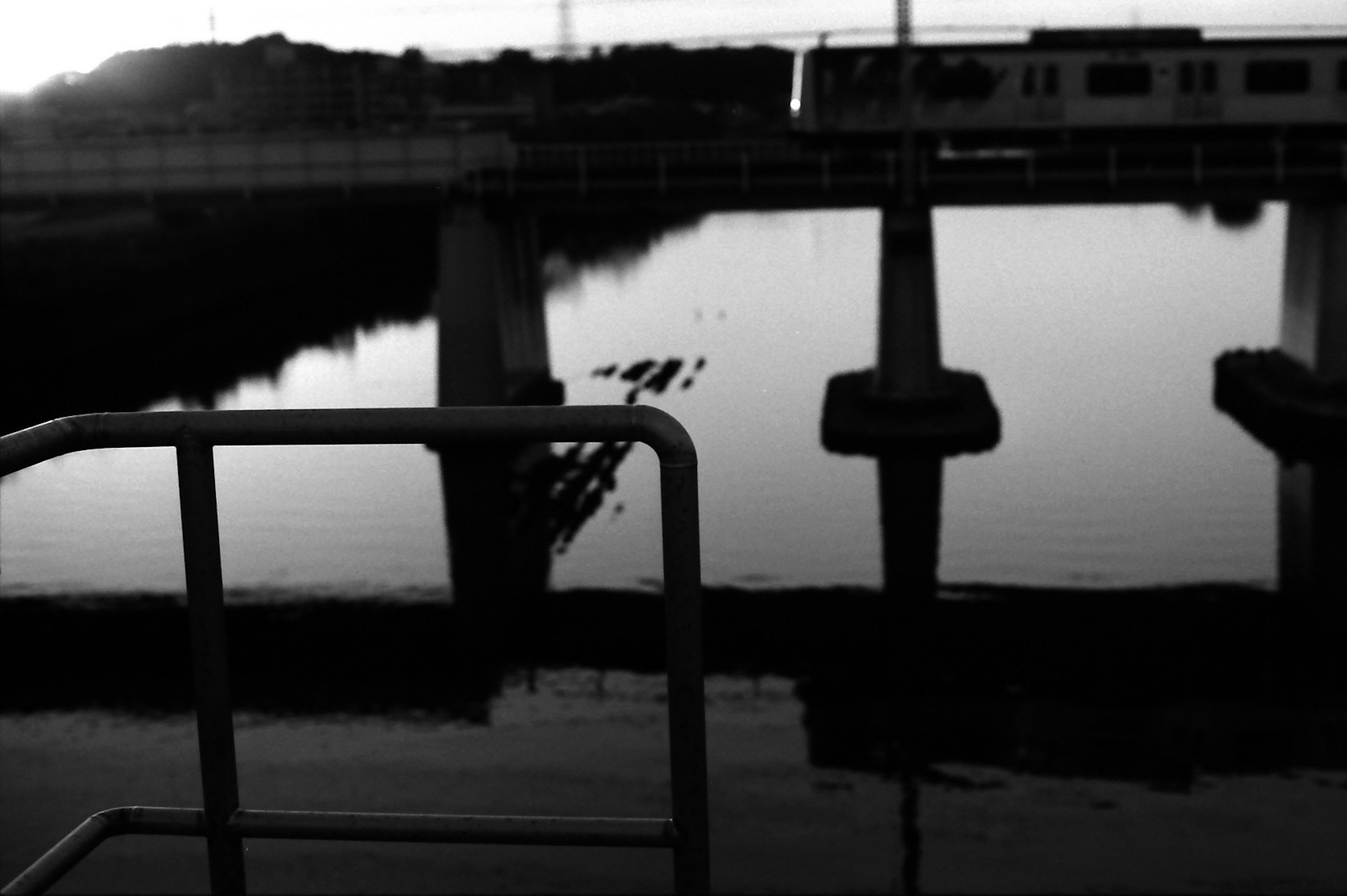 Scène de rivière en noir et blanc avec un pont ferroviaire et des reflets sur l'eau