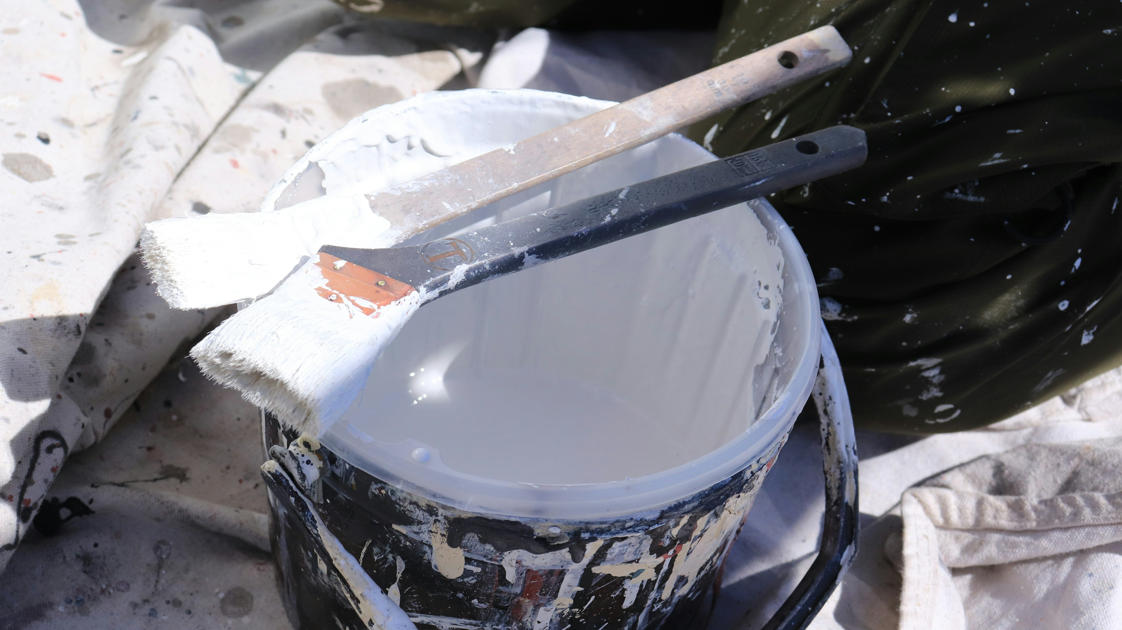 A bucket of white paint with two brushes resting on the rim