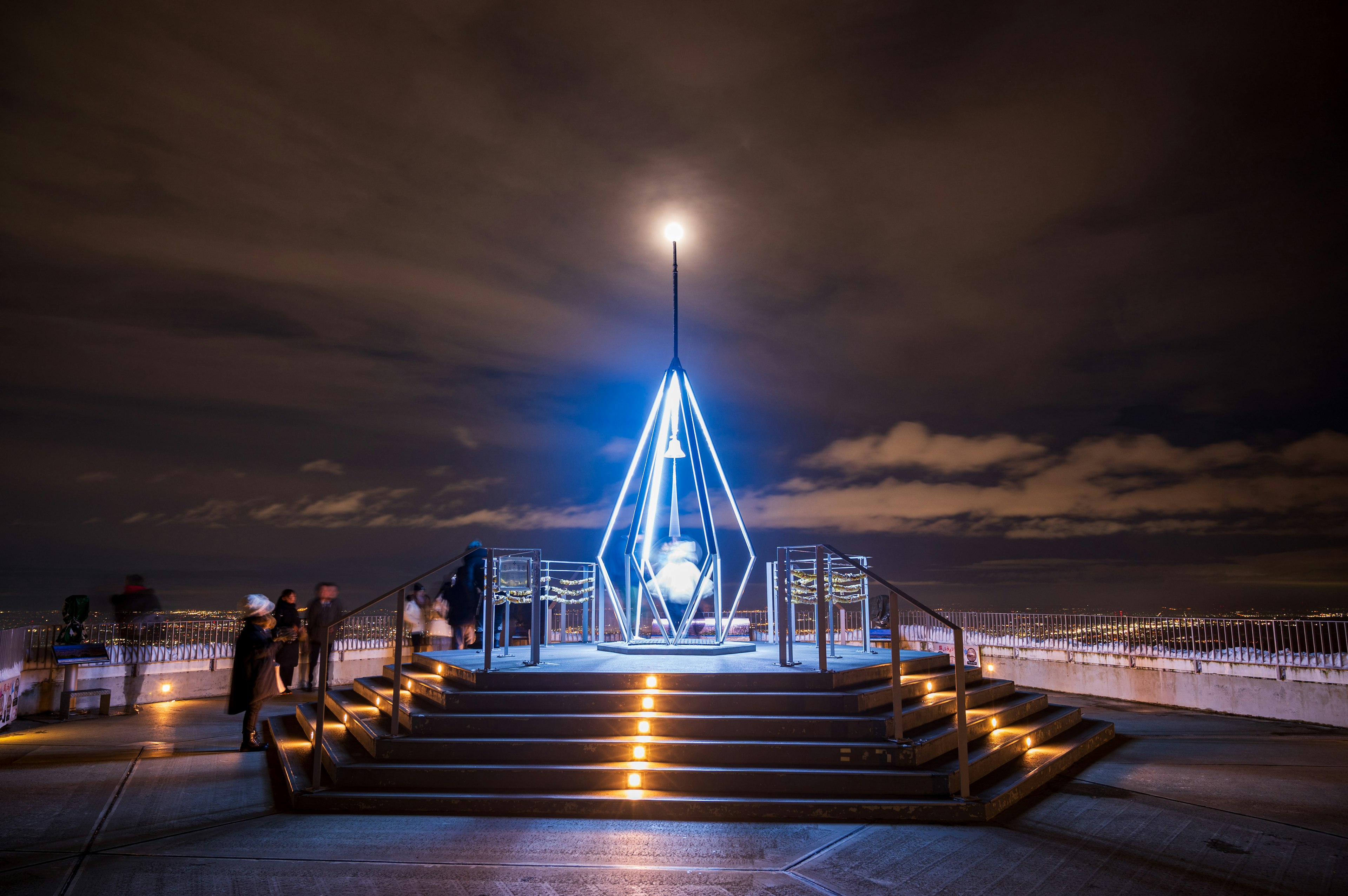 Gran escultura en forma de diamante iluminada en azul por la noche con escaleras alrededor