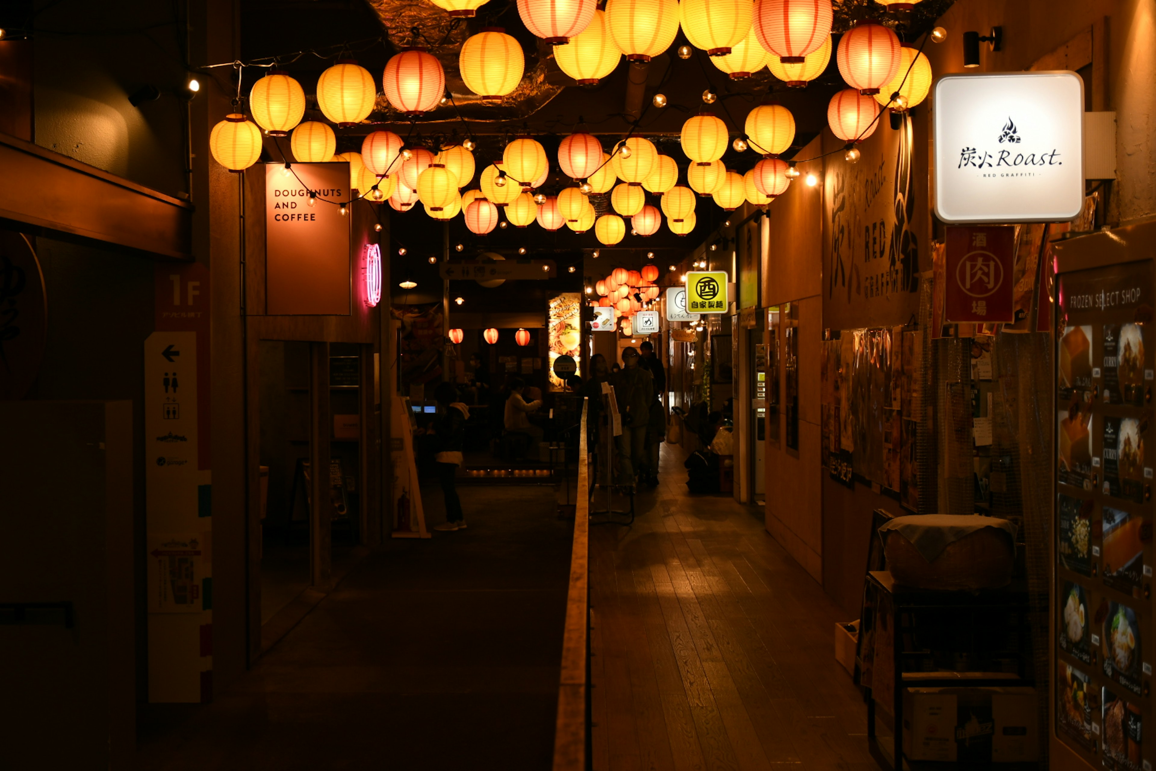 A lively street with yellow lanterns hanging above in a nighttime market