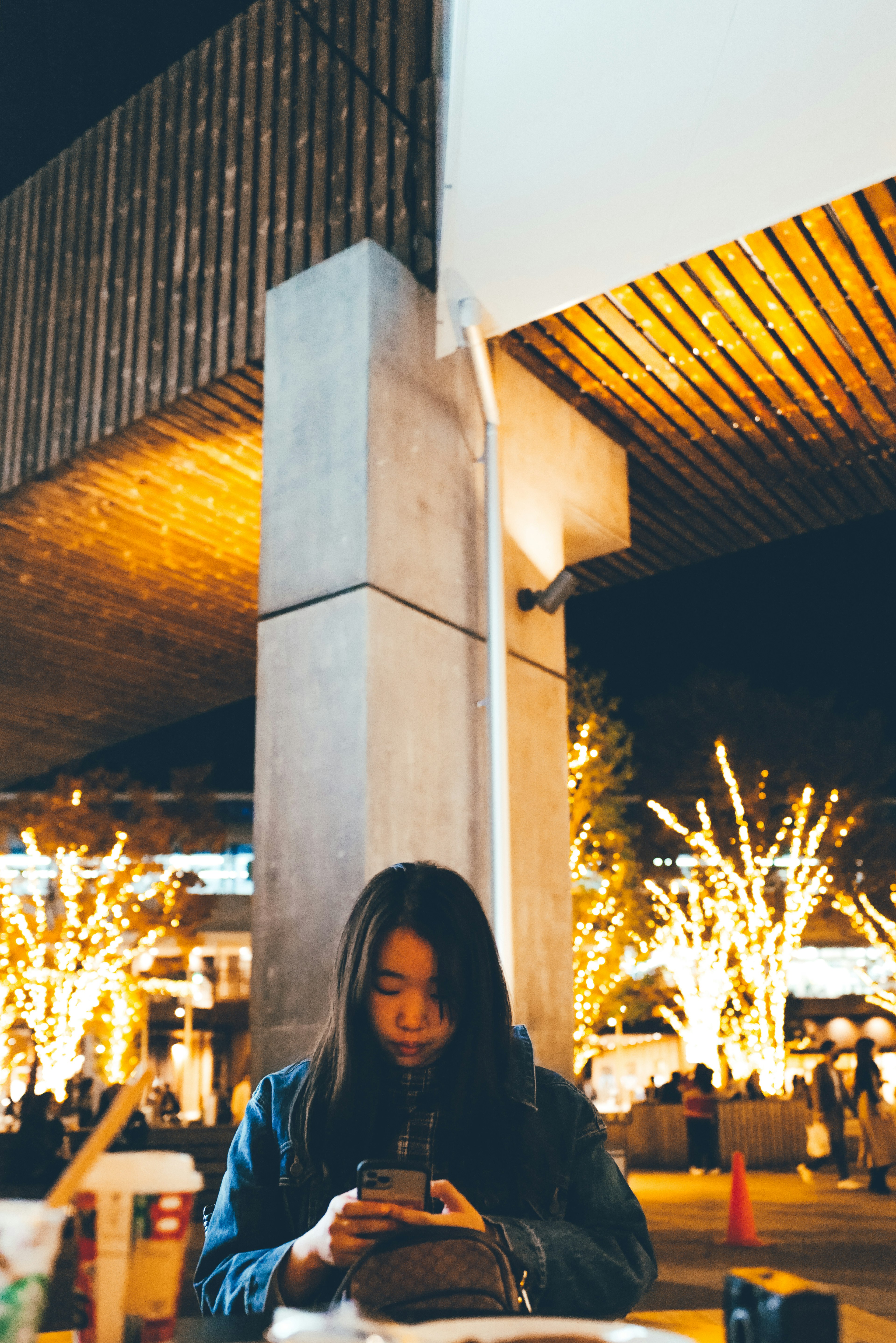 一名女性在夜间使用智能手机，背景有美丽的灯光