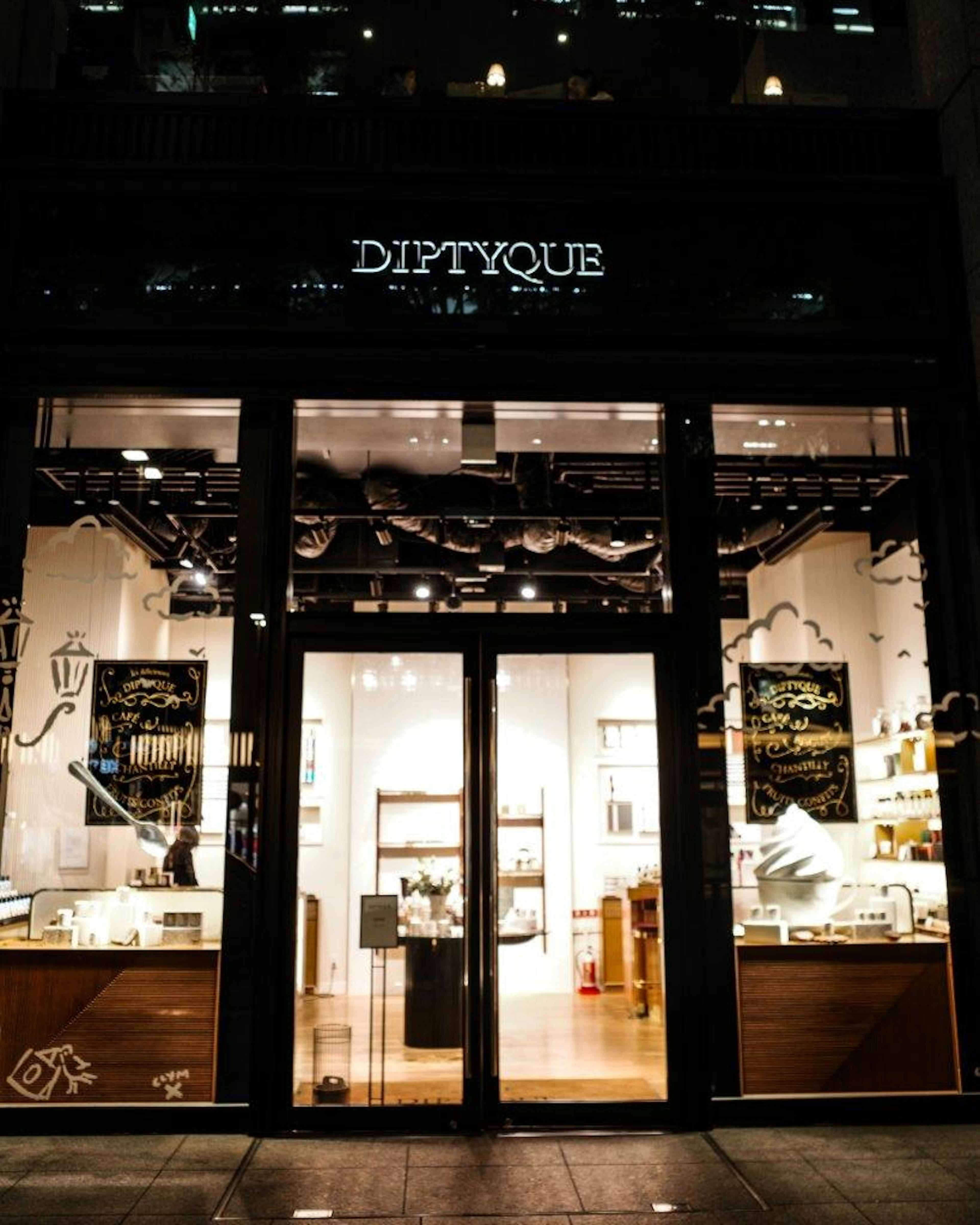 ภาพภายนอกของร้าน Diptyque มีแสงสว่างอุ่นและการออกแบบที่สง่างาม