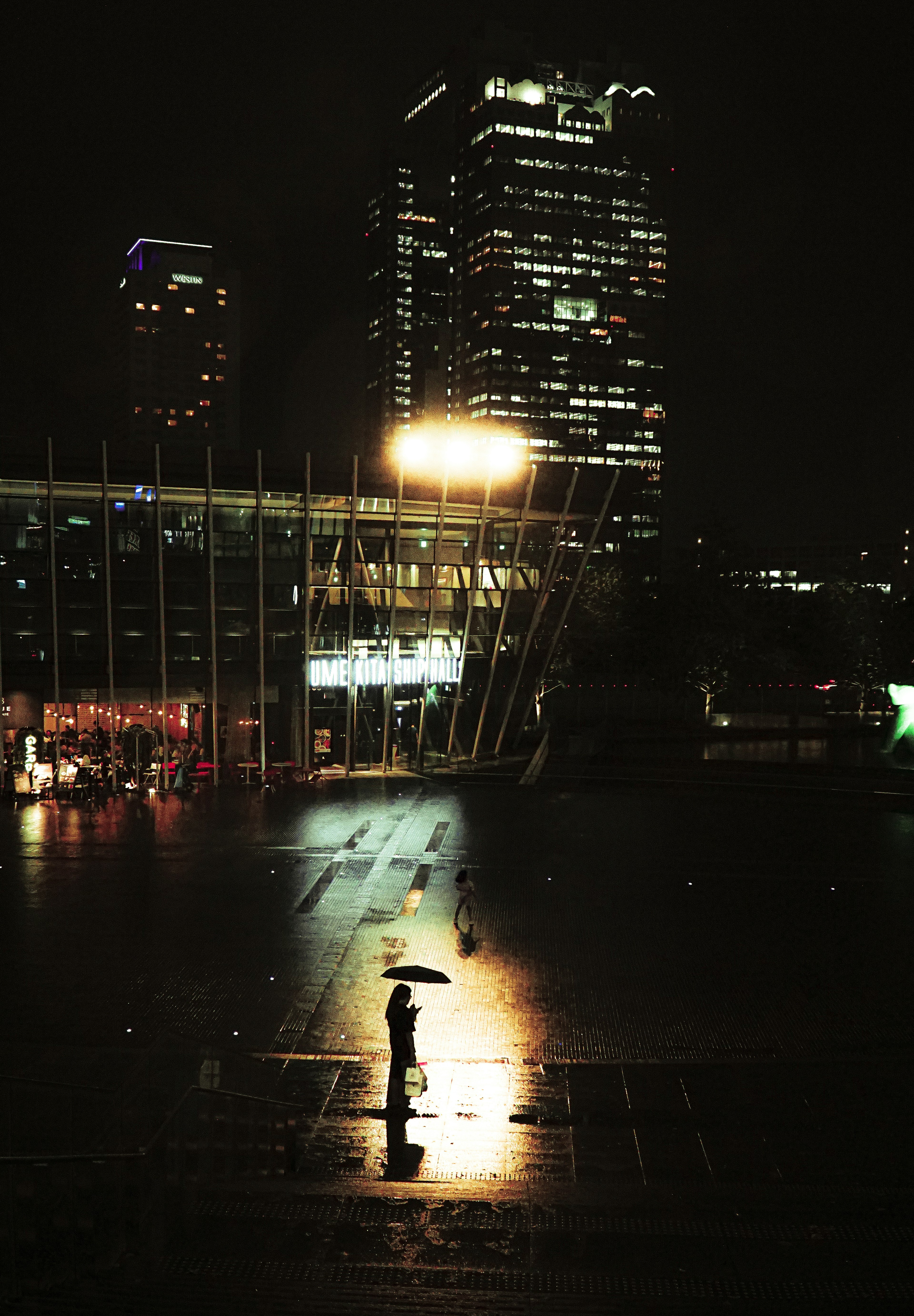 Silhouette d'une personne avec un parapluie dans une ville la nuit avec des gratte-ciel illuminés