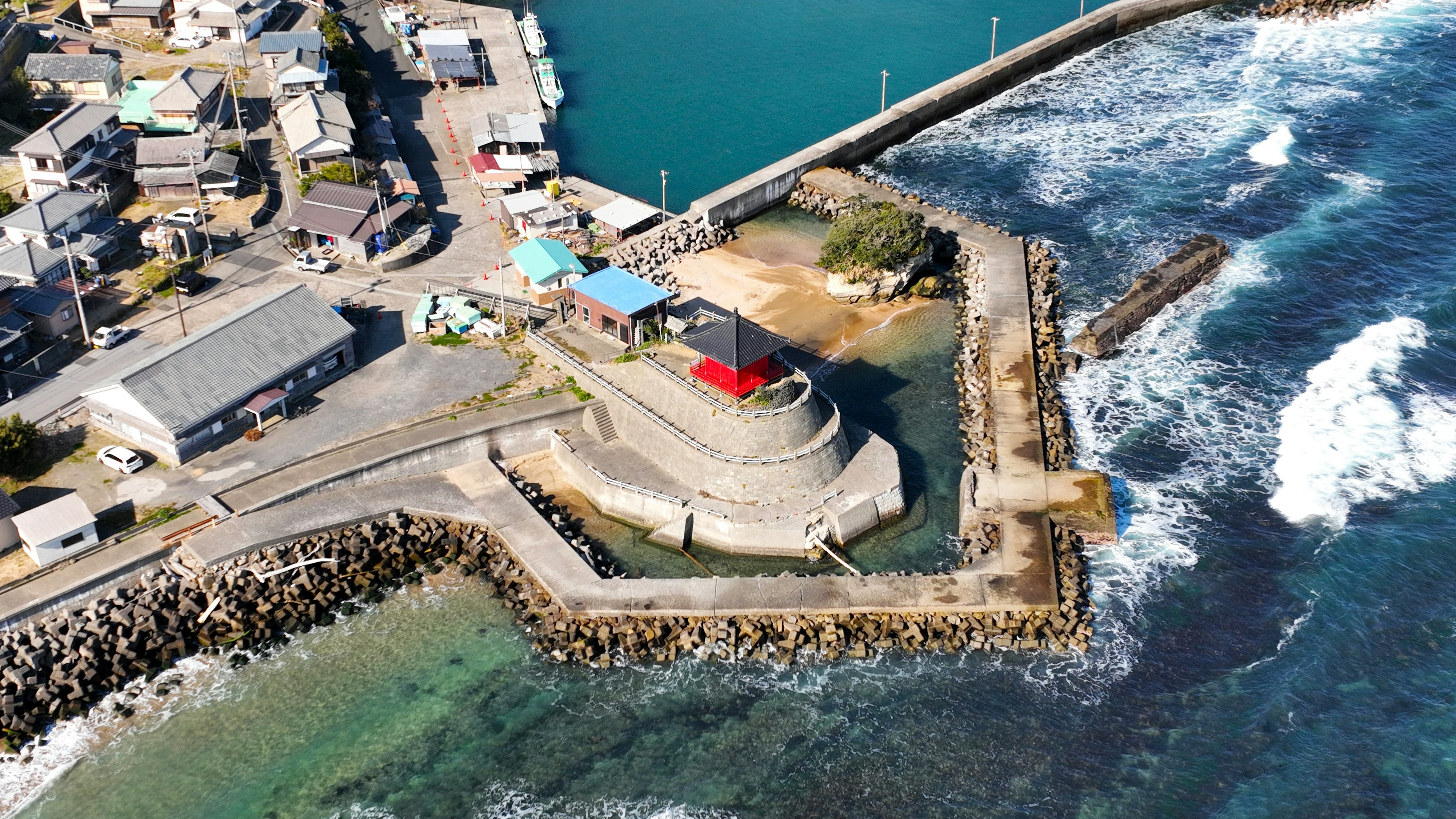 Luftaufnahme einer Küstenstadt mit einem rotbedachten Leuchtturm und brechenden Wellen am Ufer