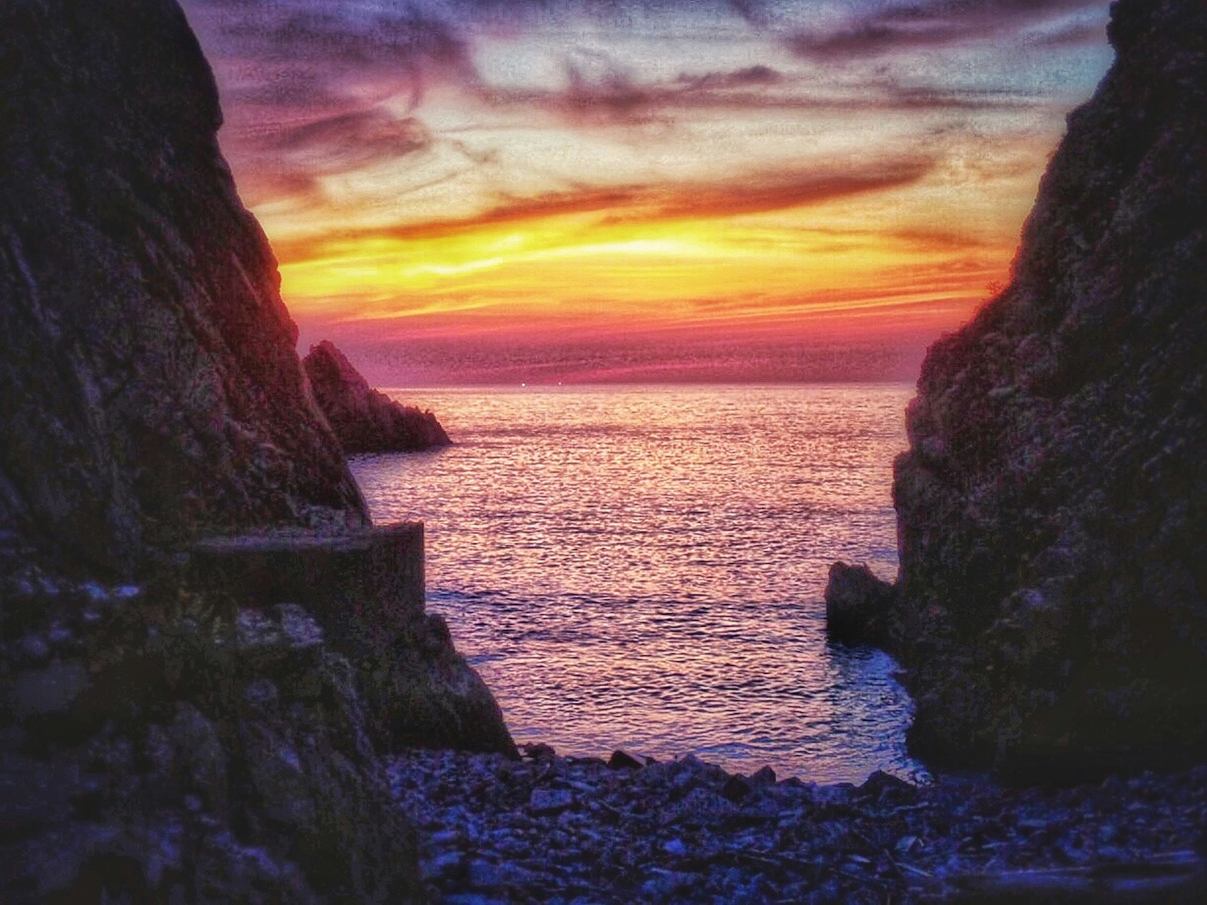 Sunset over the ocean framed by rocky cliffs