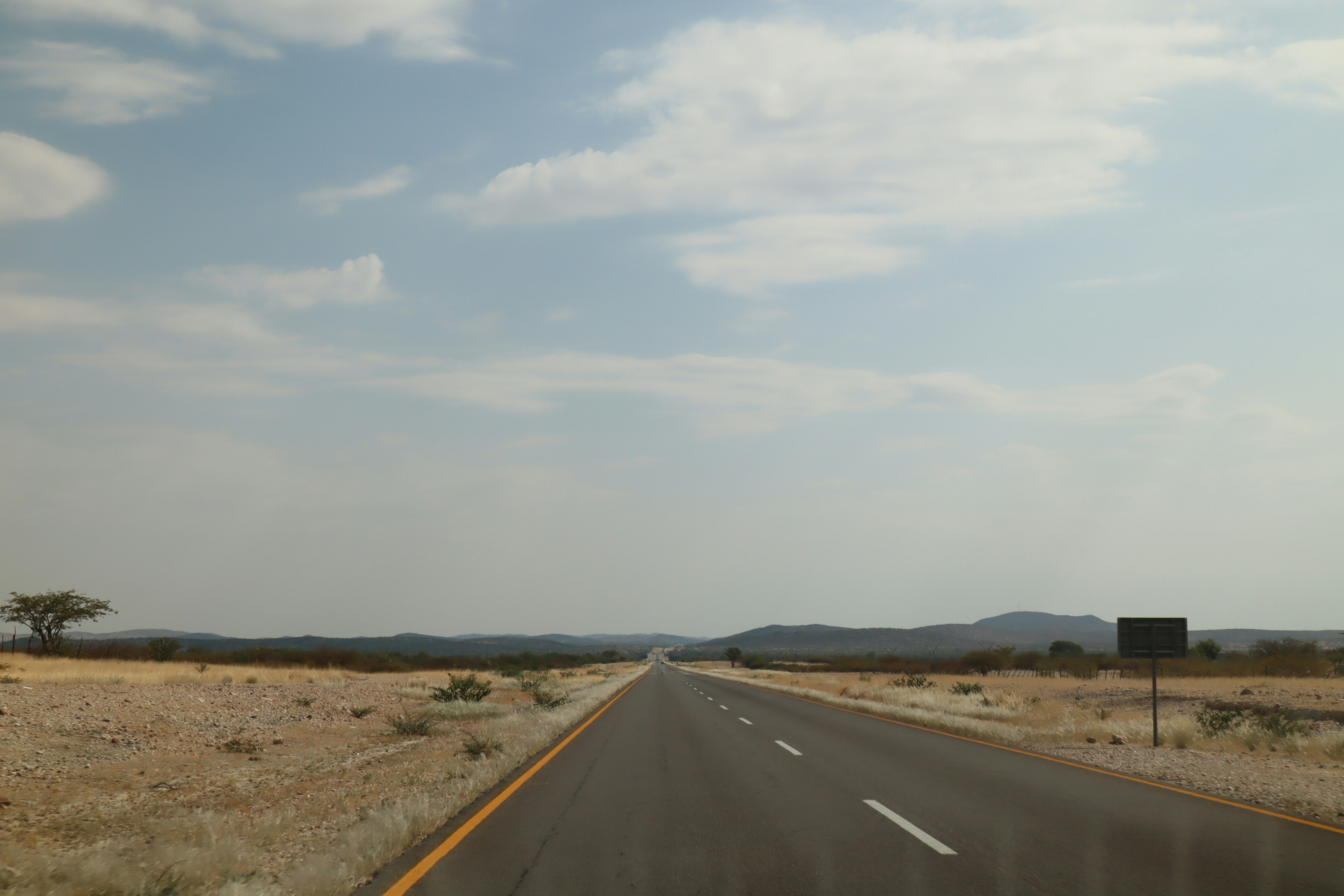 Gerade Straße, die sich durch eine trockene Landschaft unter blauem Himmel erstreckt