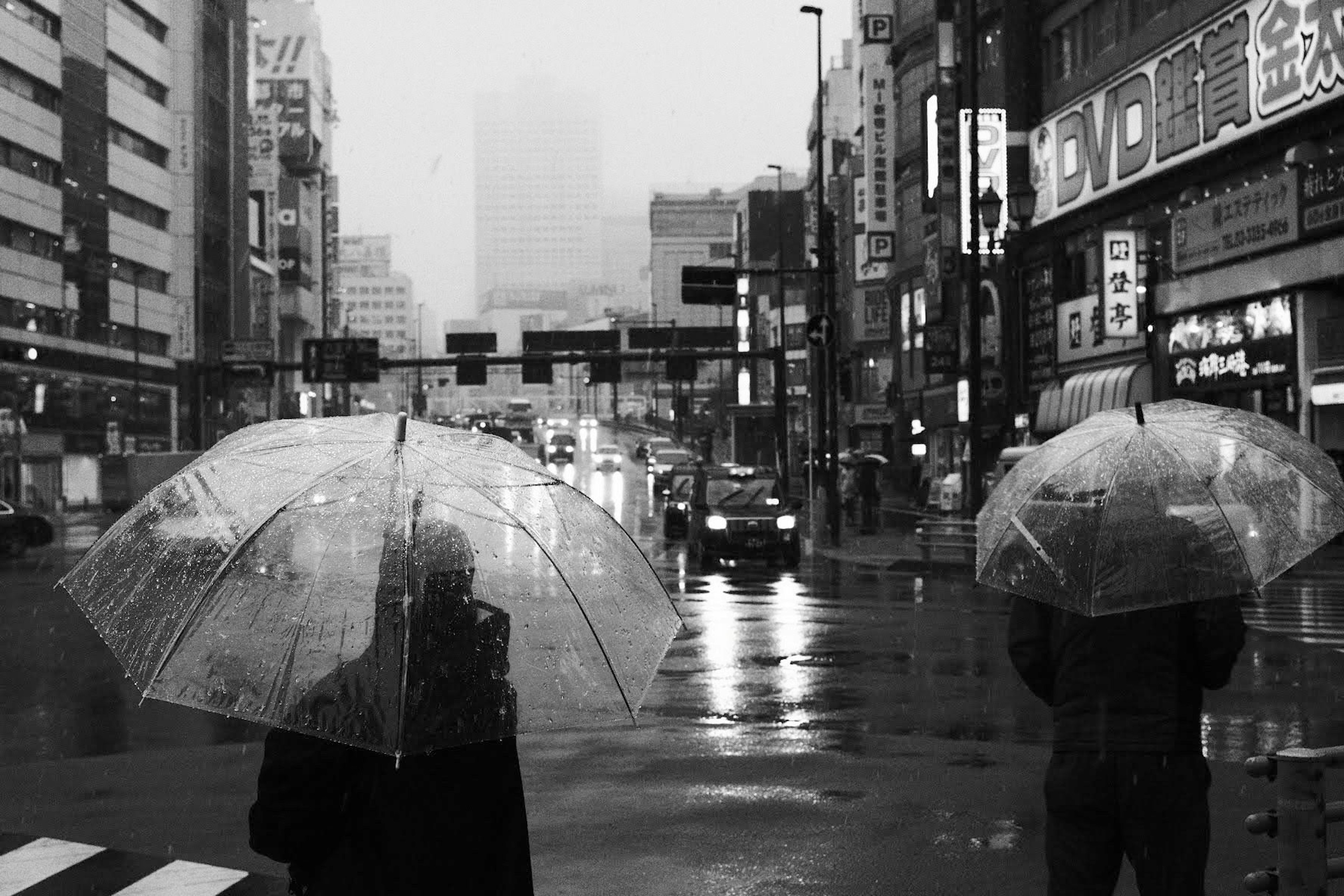 Dos personas sosteniendo paraguas transparentes de pie en un paso de peatones bajo la lluvia