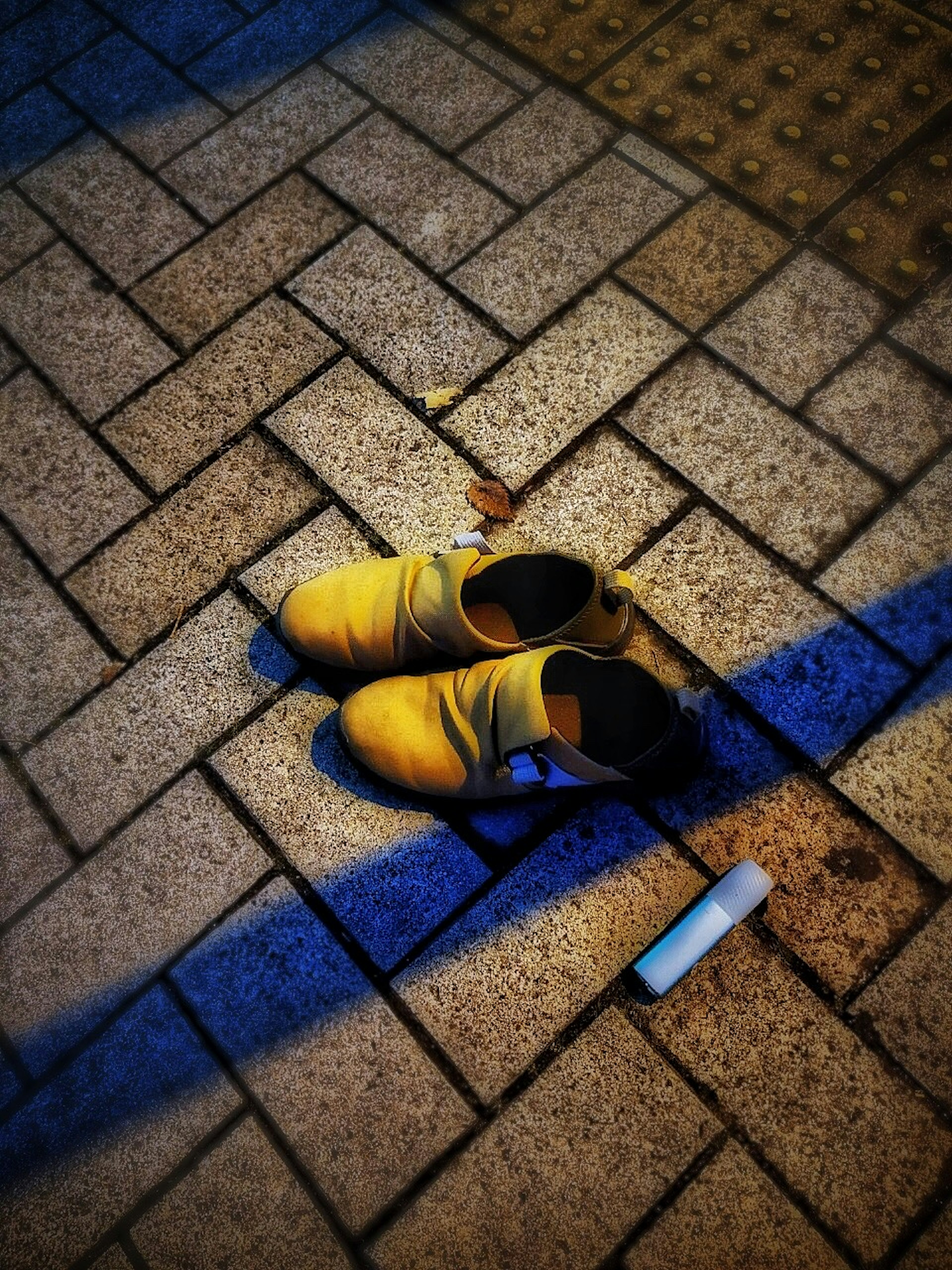 A pair of yellow shoes placed on tiled pavement