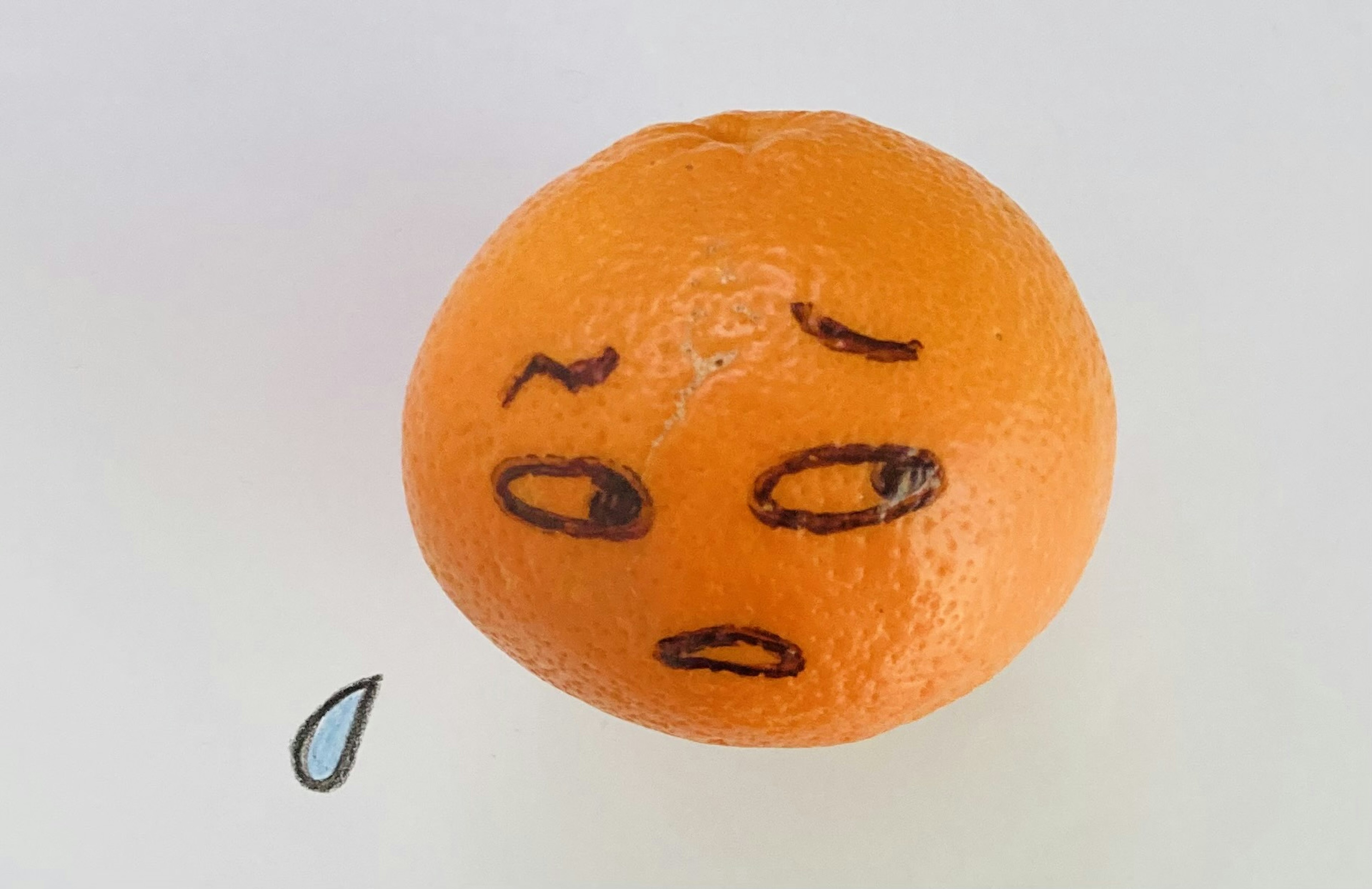 An orange with a face drawn on it and a teardrop