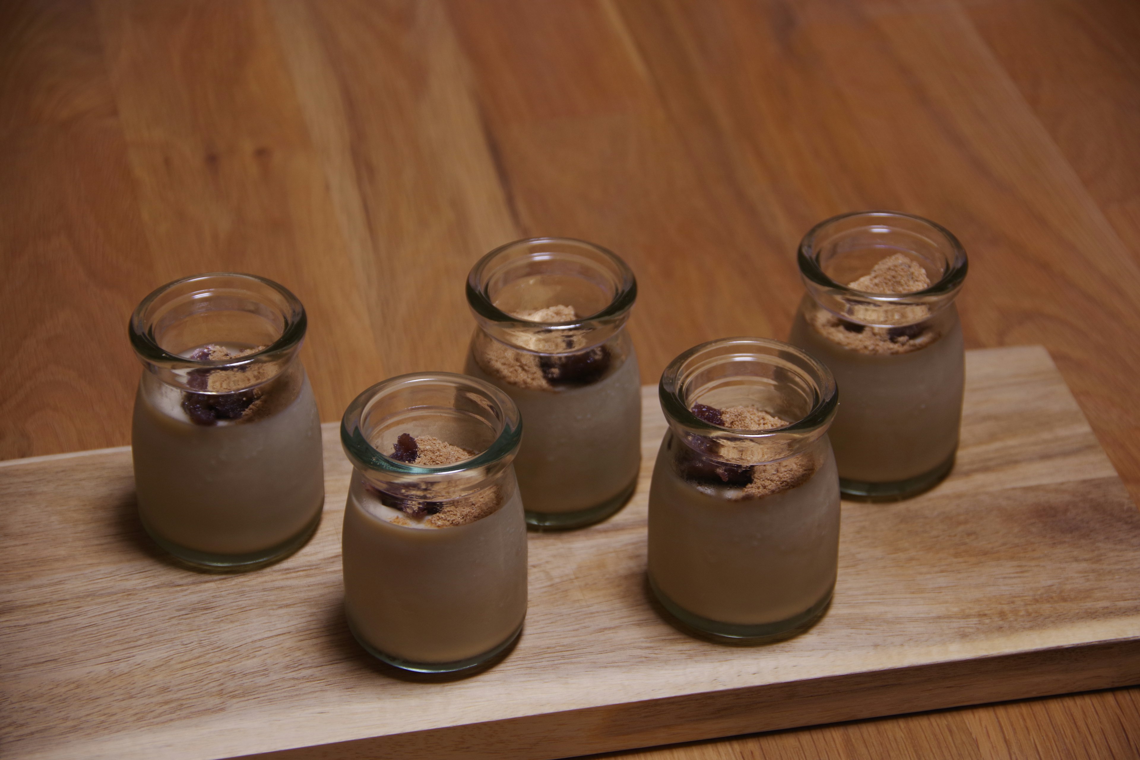 Fünf Dessertgläser mit cremigem Pudding auf einem Holzbrett