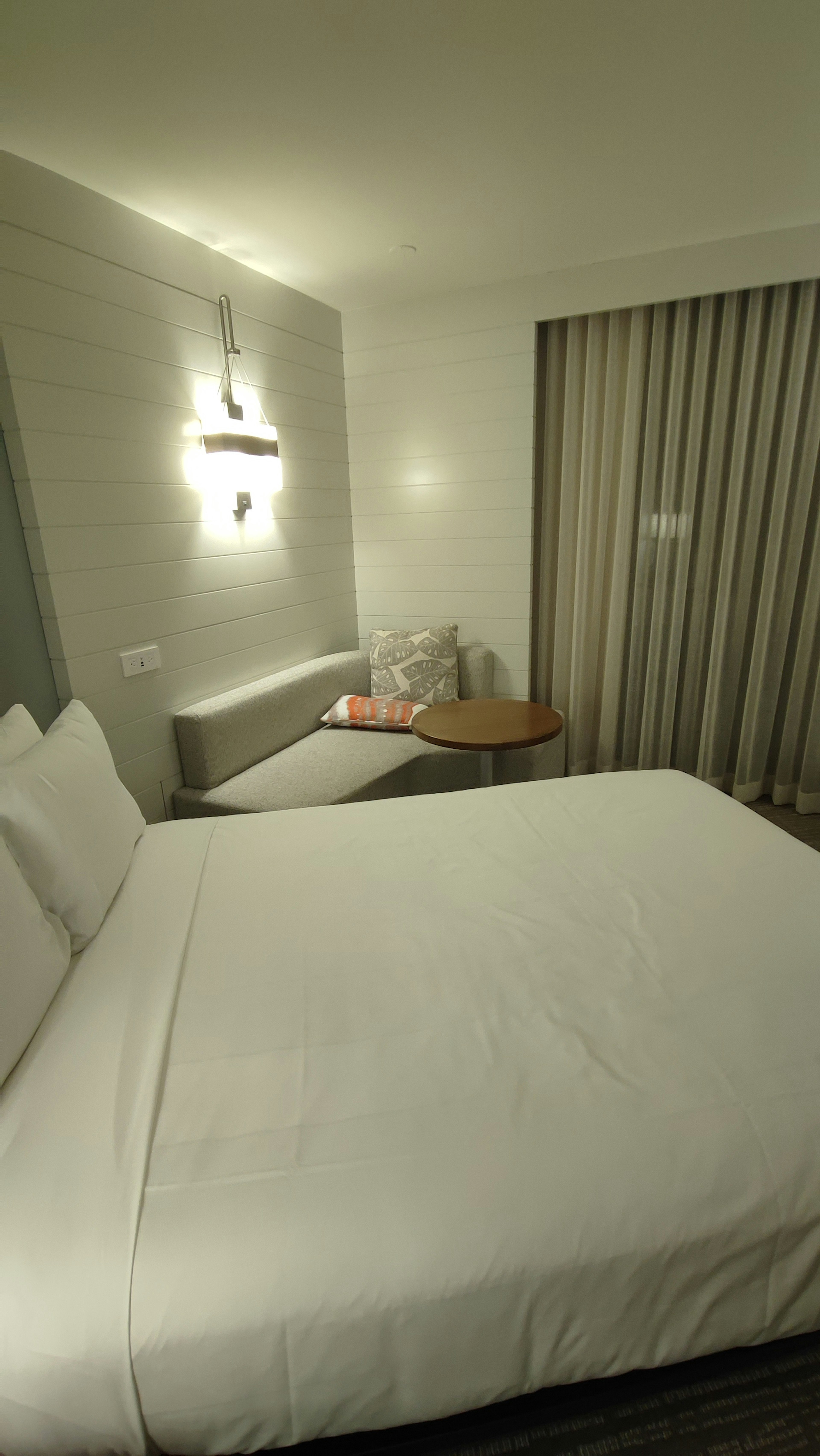 Habitación de hotel moderna con cama blanca y almohadas suaves iluminación de pared y cortinas en la ventana