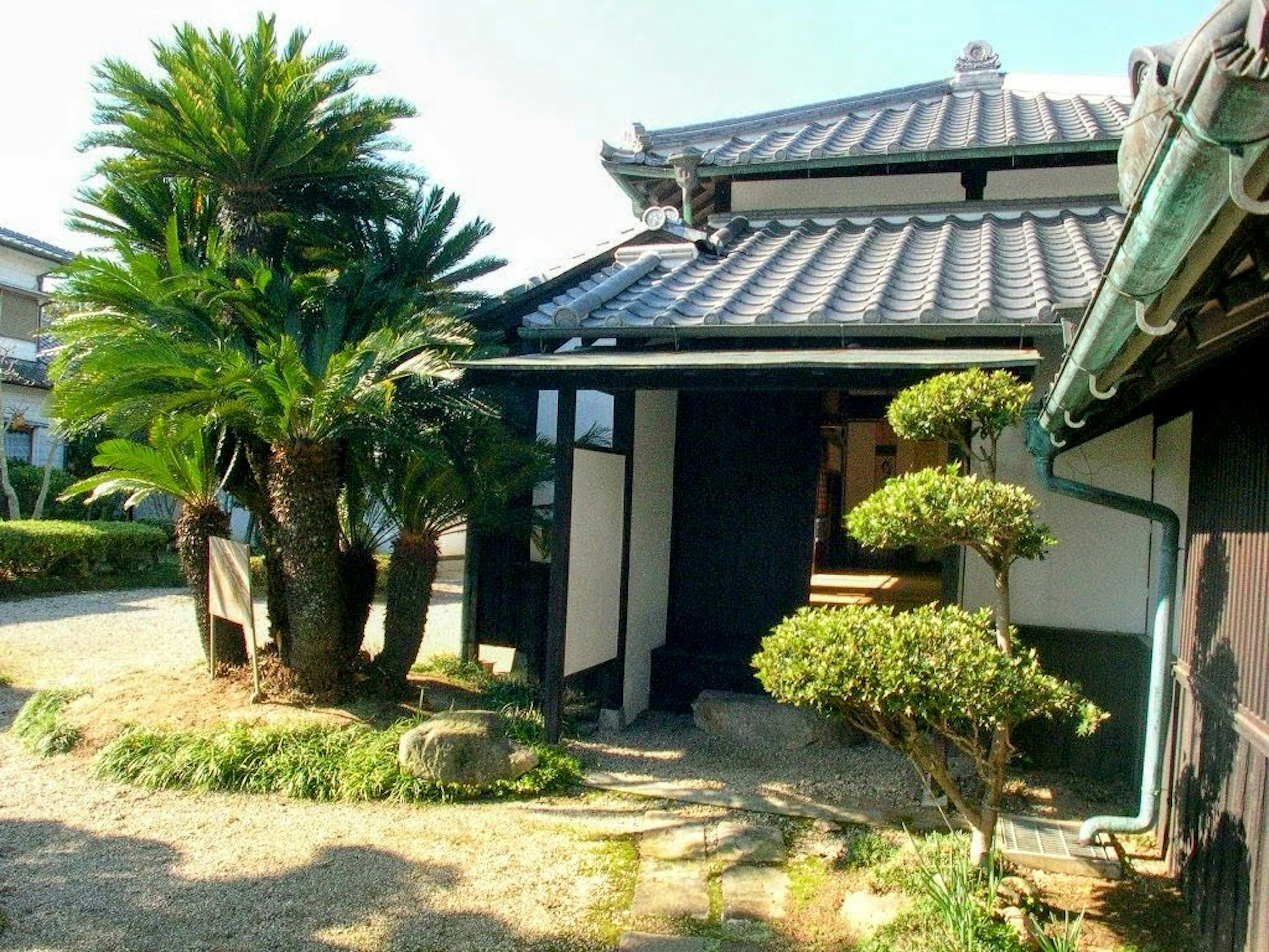 Maison japonaise traditionnelle avec un jardin présentant des palmiers et des buissons taillés