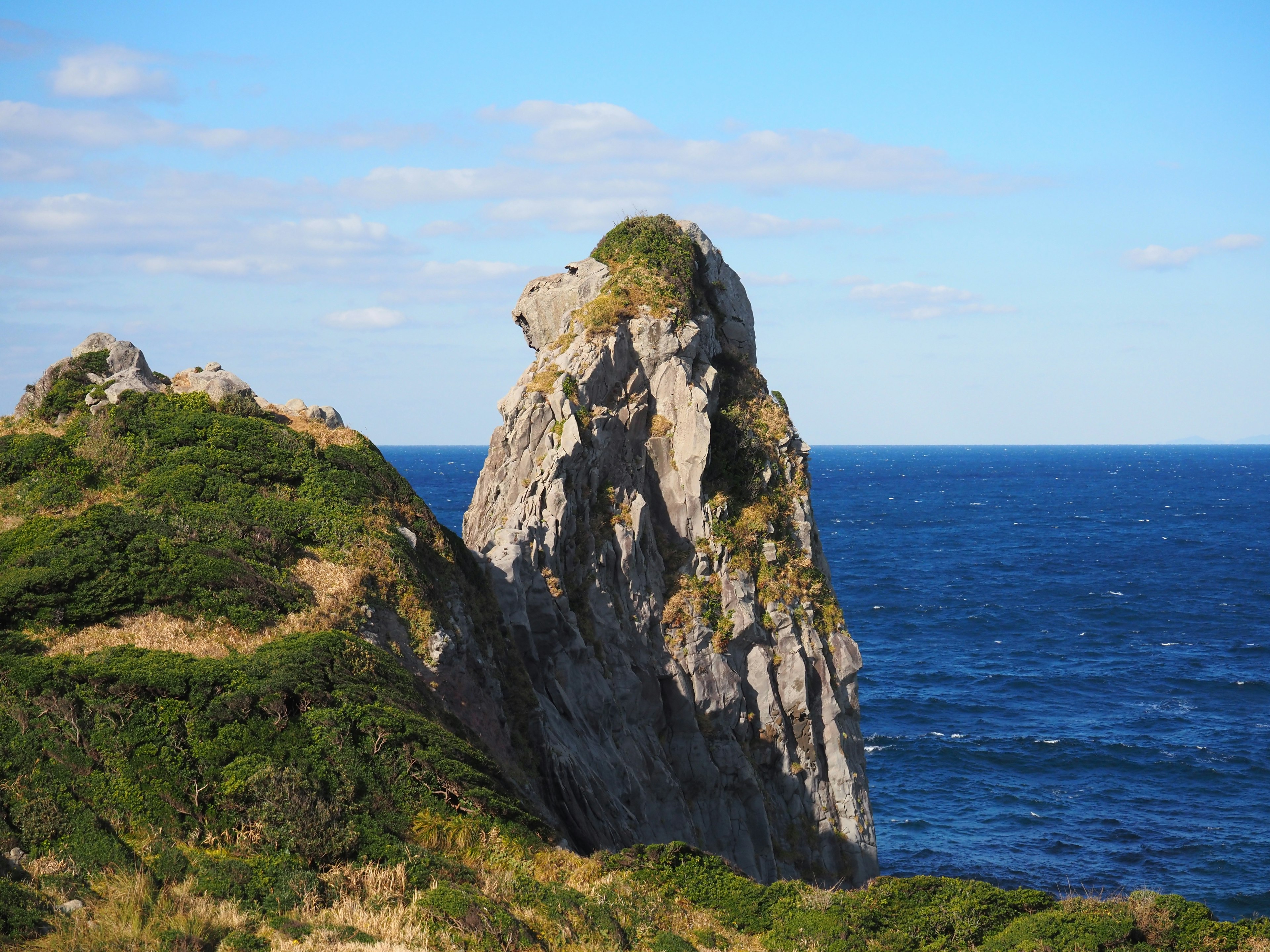 A rocky pinnacle rising from a green hillside overlooking the ocean