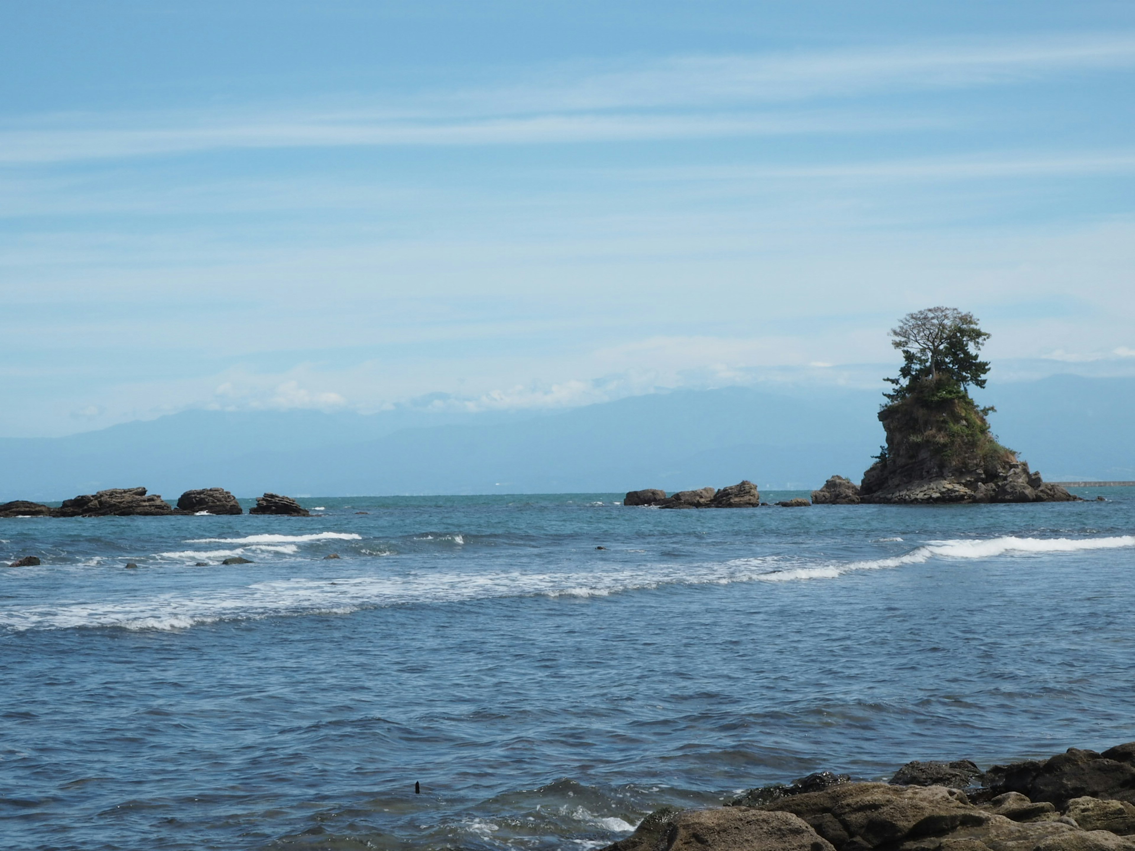 Una pequeña isla con un árbol bajo un cielo azul y olas oceánicas