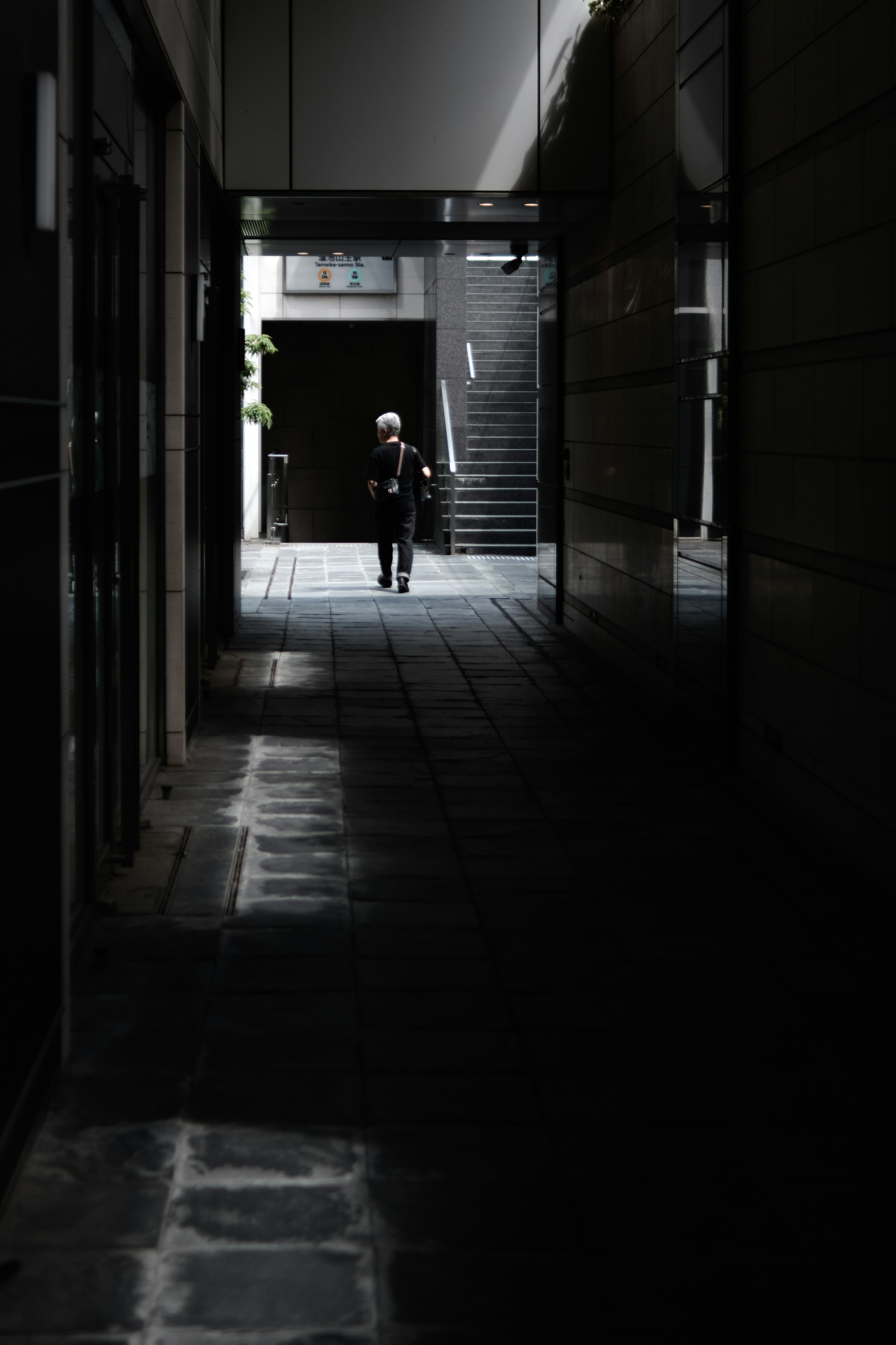 Silhouette einer Person, die in einer schwach beleuchteten Gasse geht Helle Treppe im Hintergrund