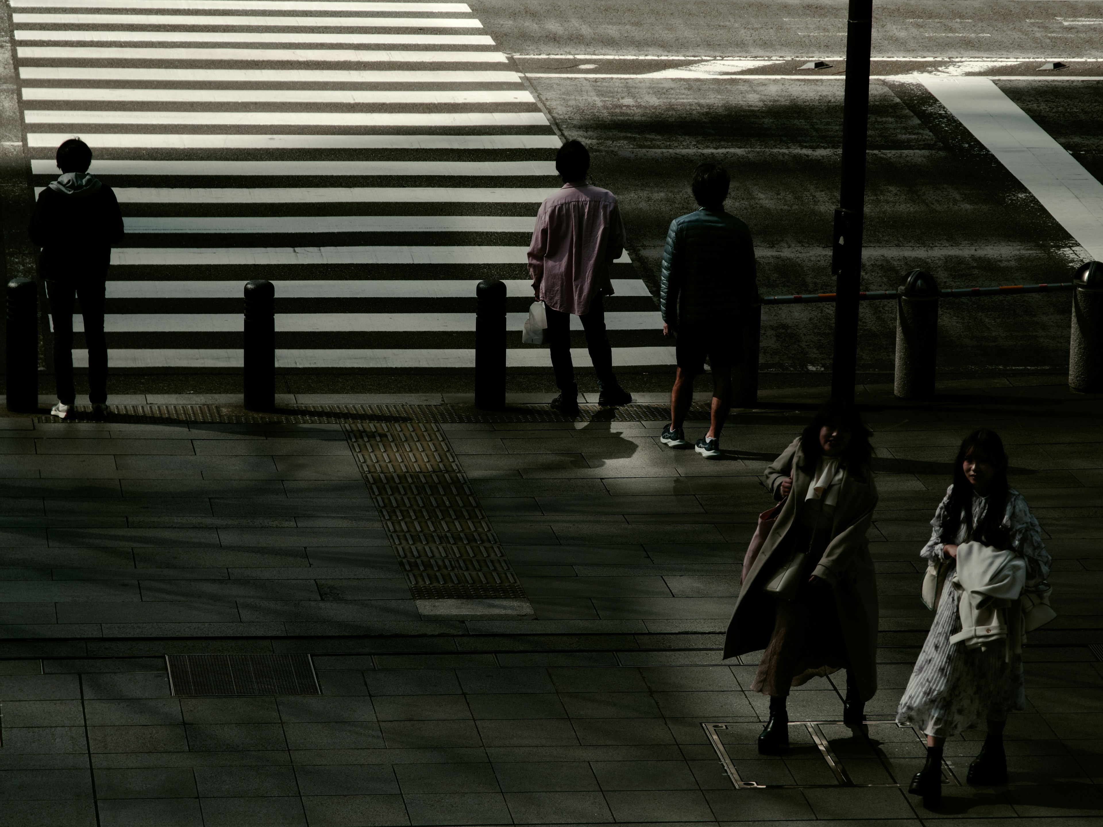 Silhouettes de personnes attendant à un passage piéton avec des bandes blanches