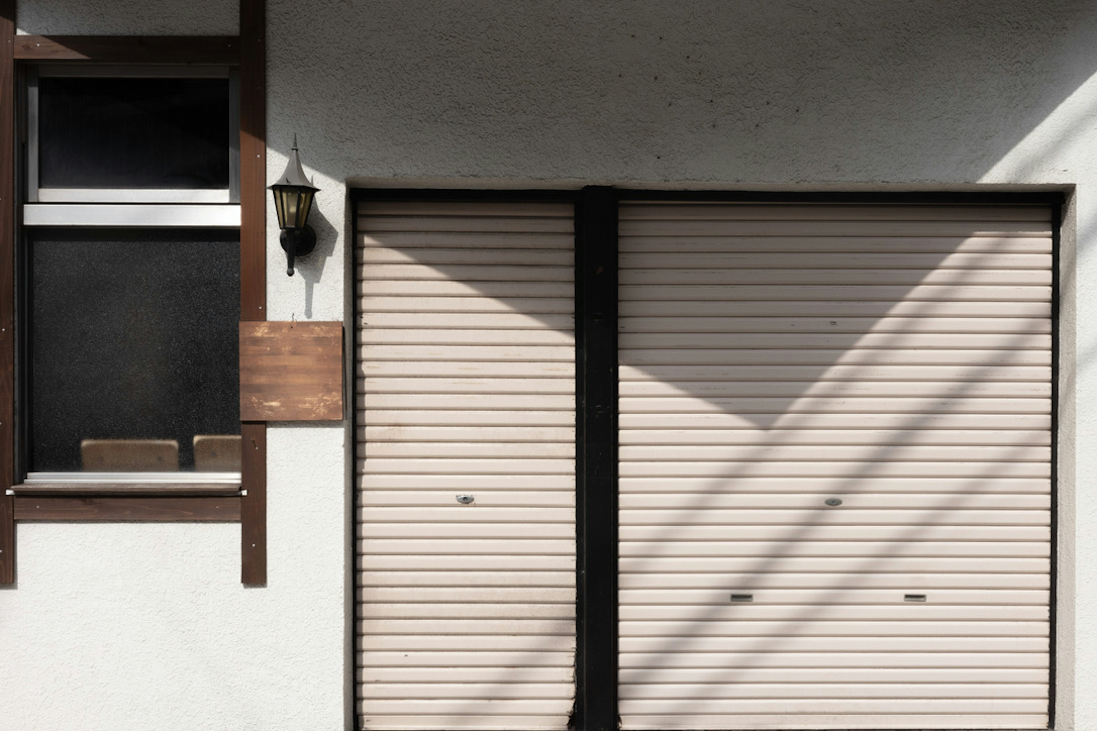 Extérieur d'un garage avec un mur blanc une fenêtre en bois et des volets roulants