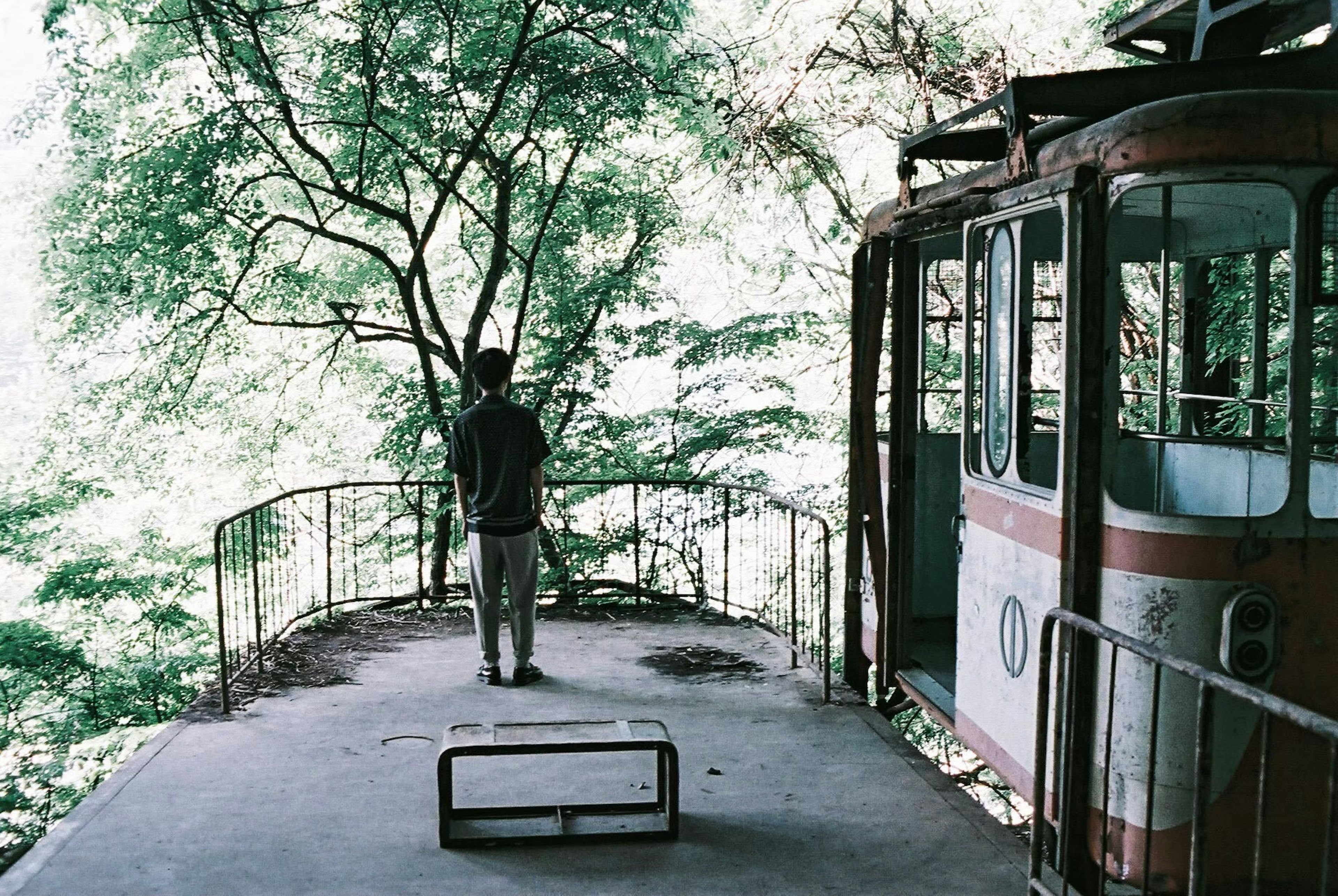 A person standing on an abandoned trolley platform surrounded by green trees