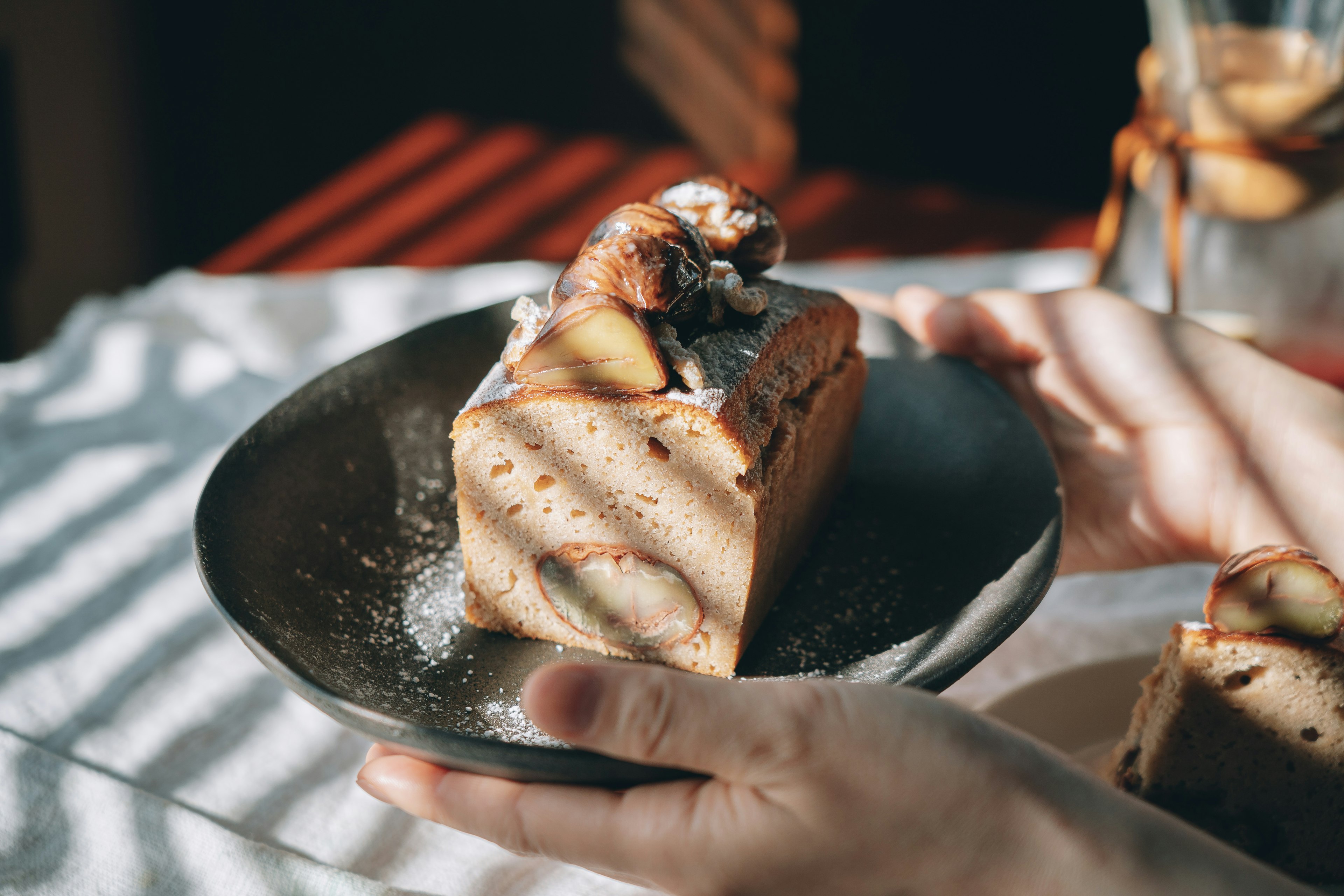 Una mano sosteniendo una rebanada de pastel en un plato negro con sombras hermosas