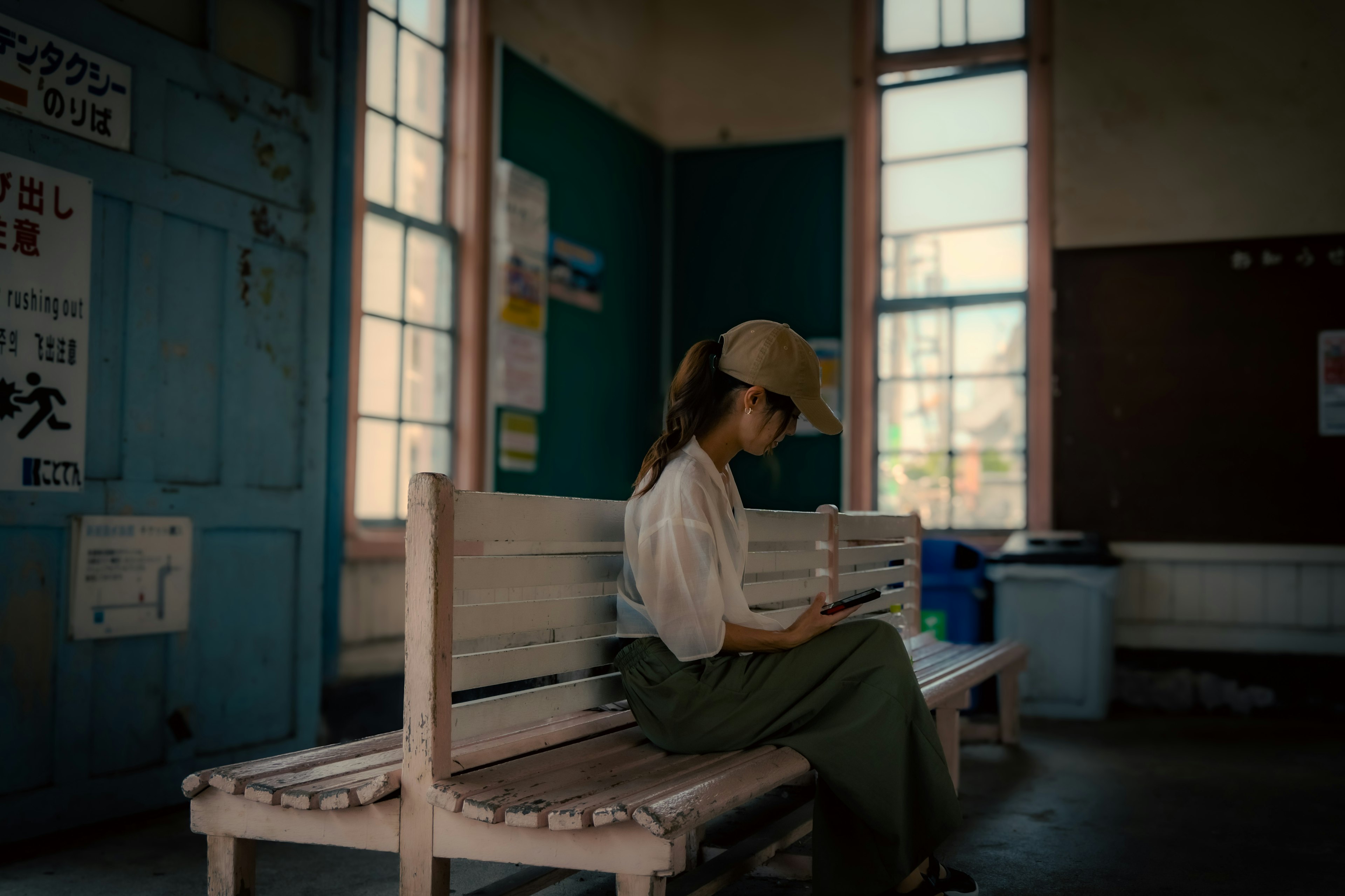 Une femme assise dans une salle d'attente de gare tranquille portant une casquette et regardant son smartphone