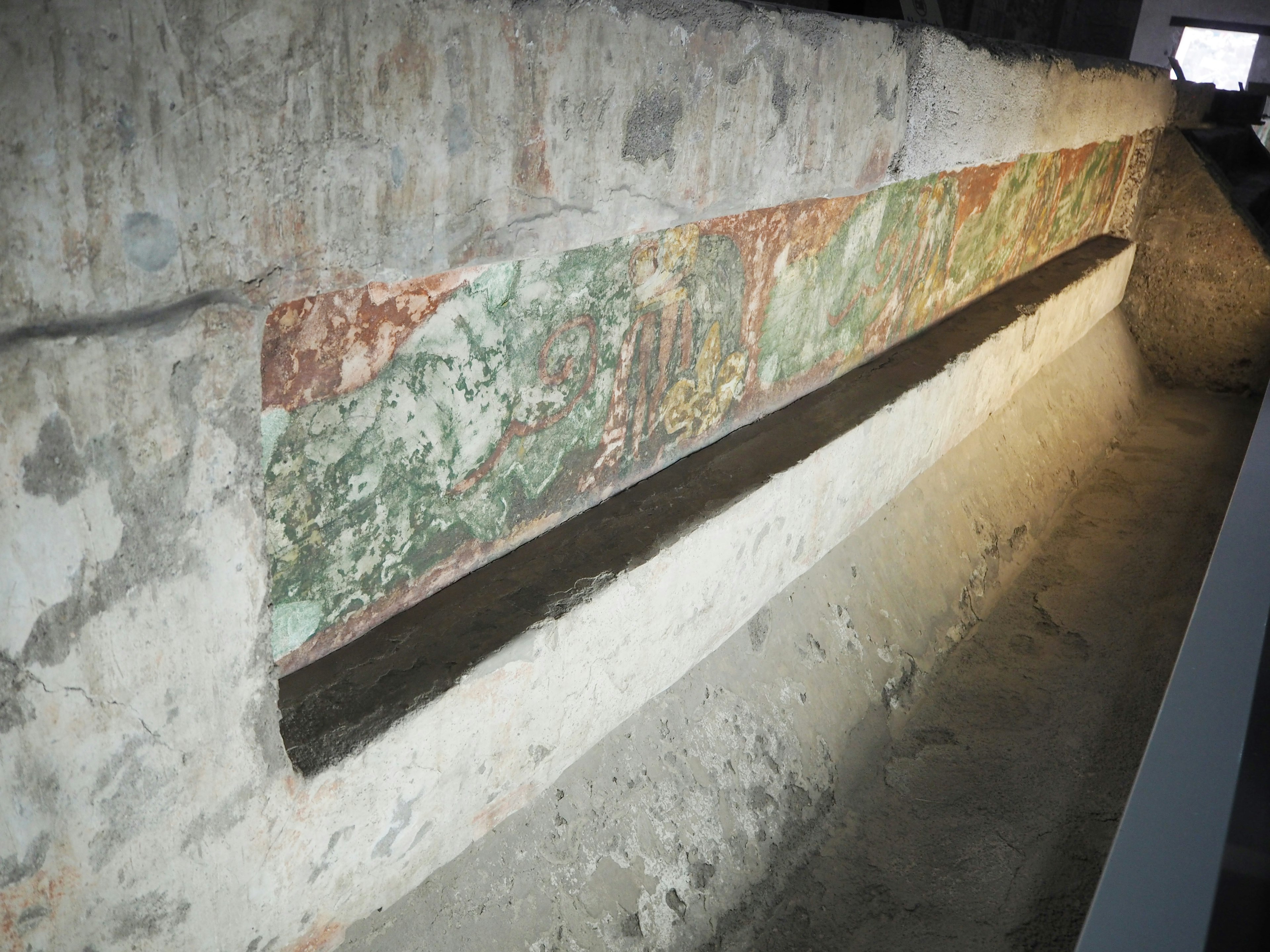 Section exposée d'un mur ancien avec des décorations vertes et rouges fanées