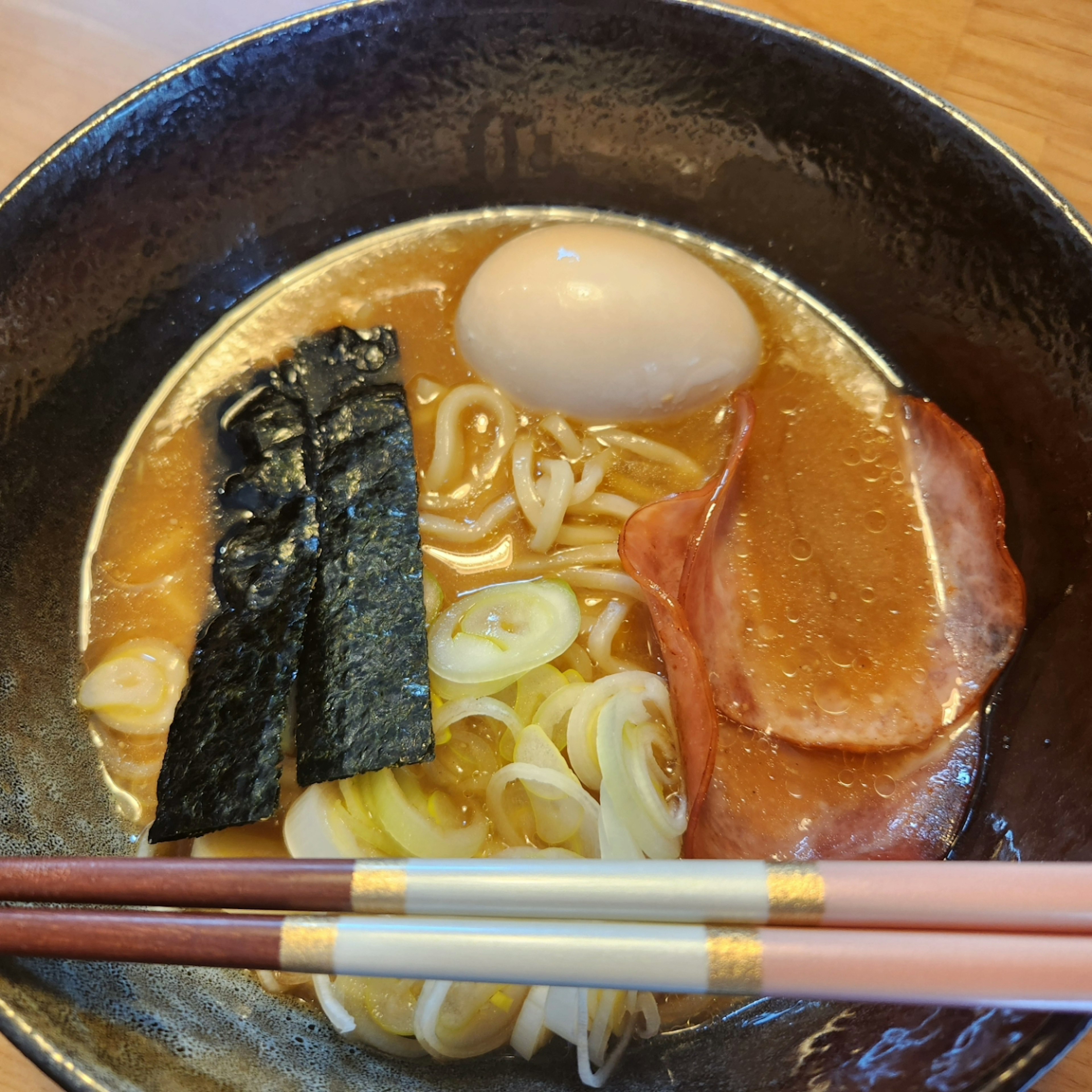 Una ciotola di ramen con brodo, noodles, uovo e condimenti