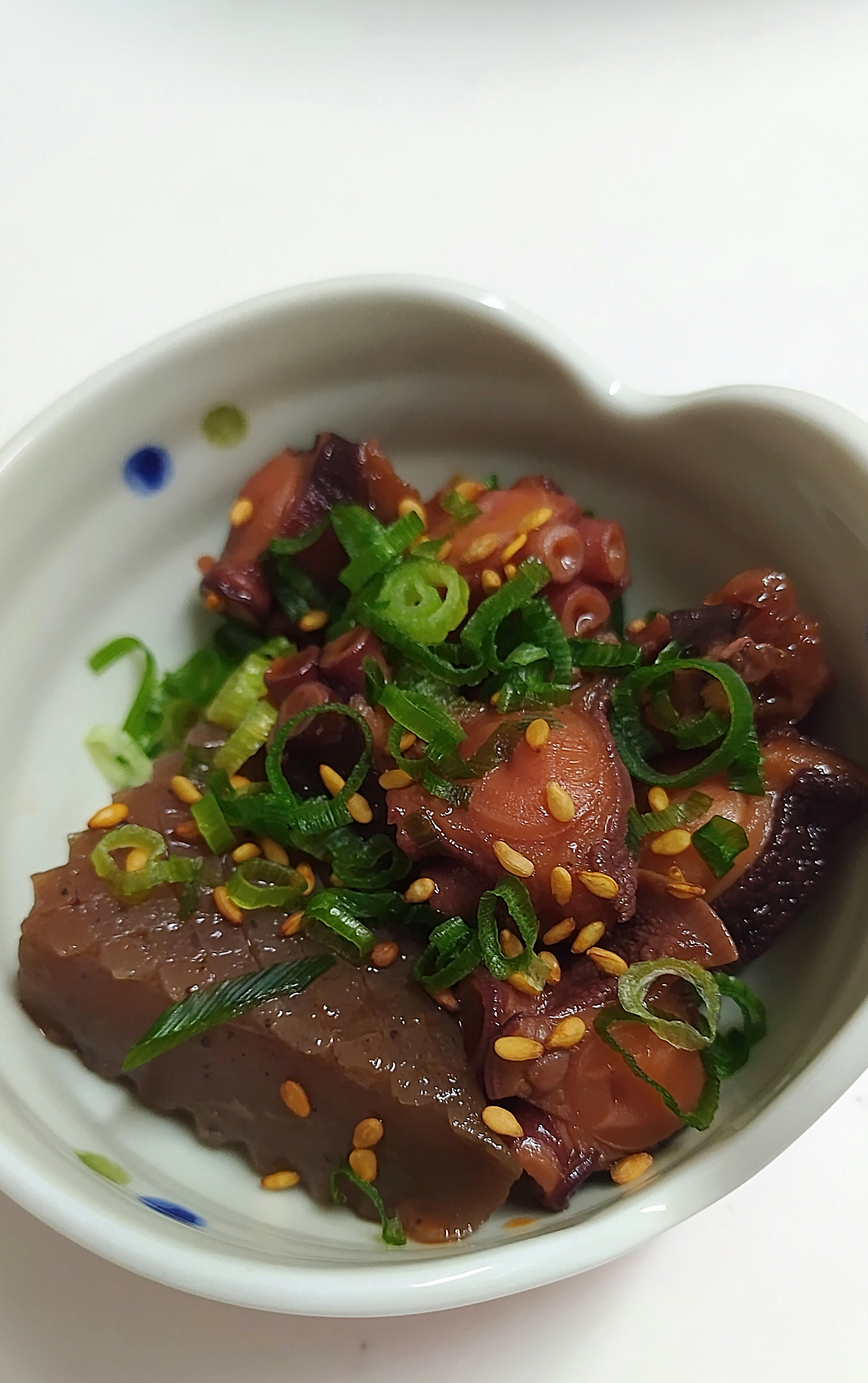 A delicious pork dish served in a small bowl garnished with green onions and sesame seeds